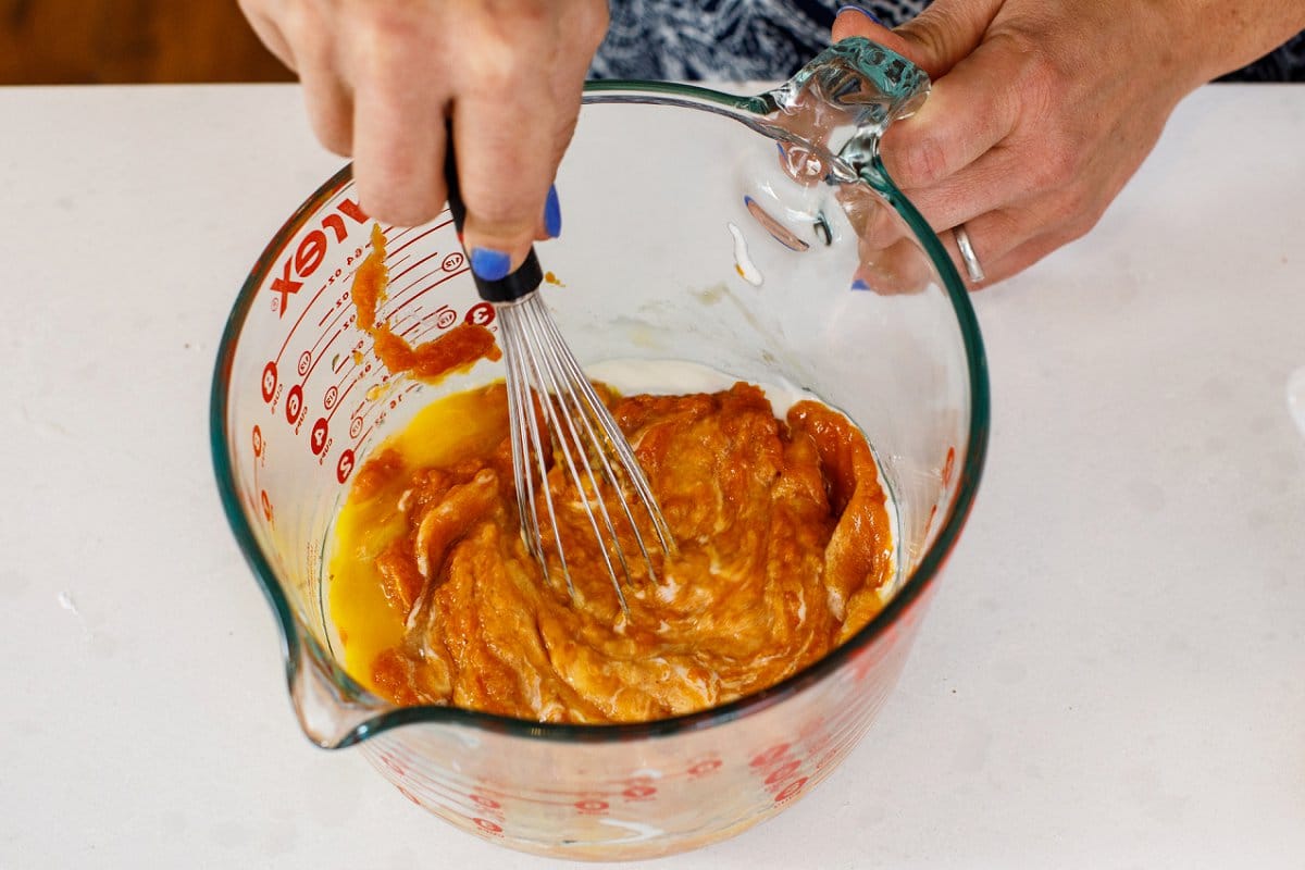 Liz's hand whisking wet ingredients inside a large glass measuring cup