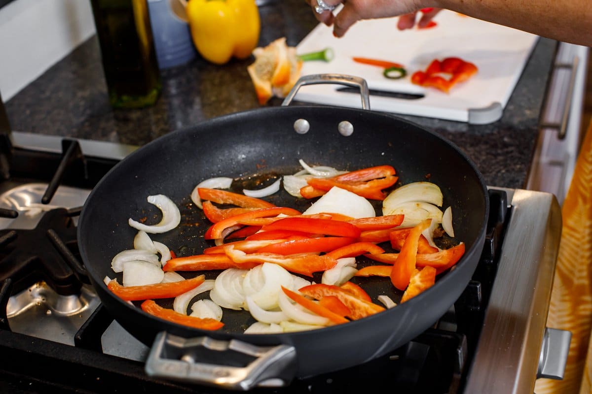 Adding sliced red pepper and sliced white onion to a hot skillet.