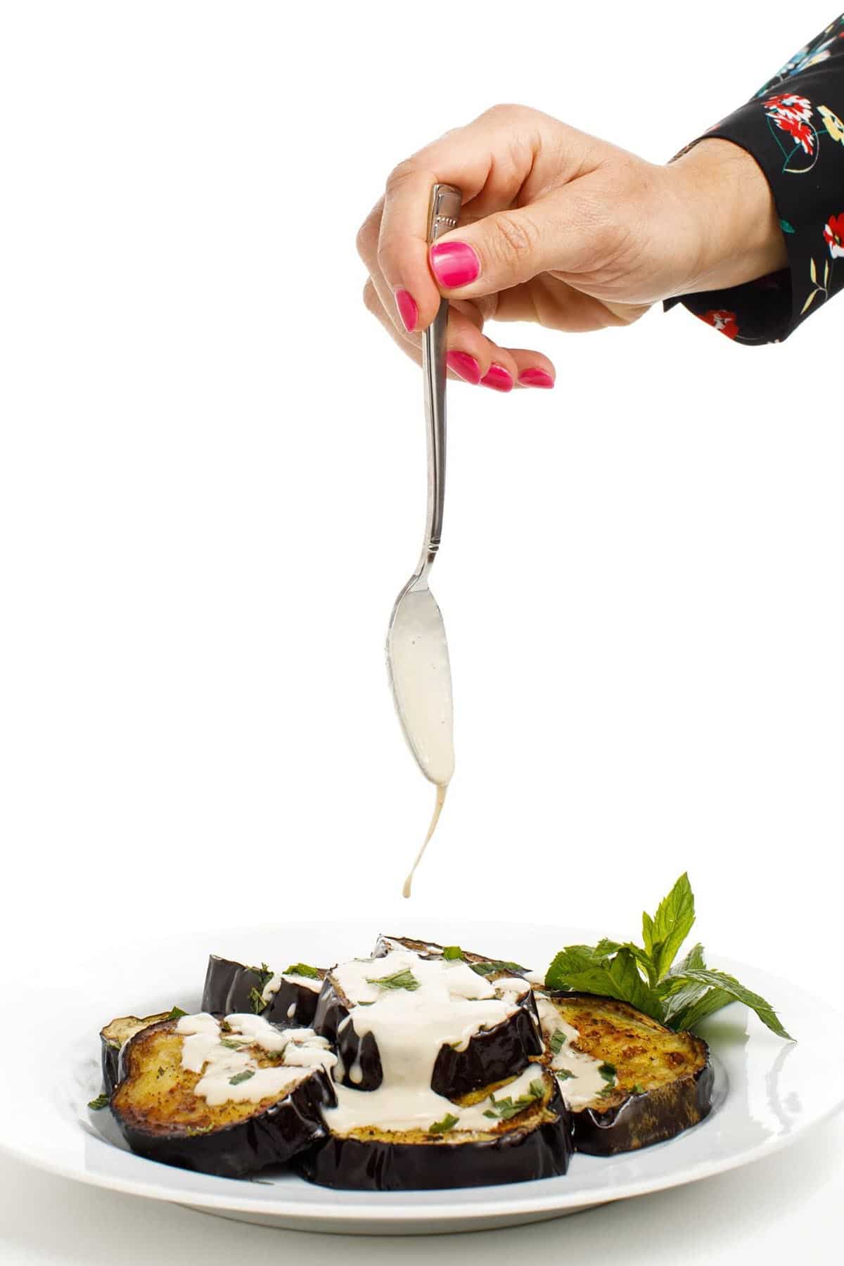 Drizzling tahini sauce on grilled eggplant.