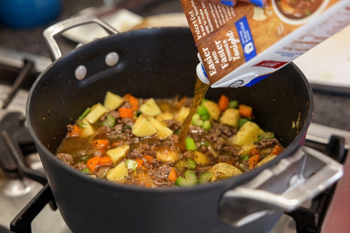 Adding beef broth to soup in a pot