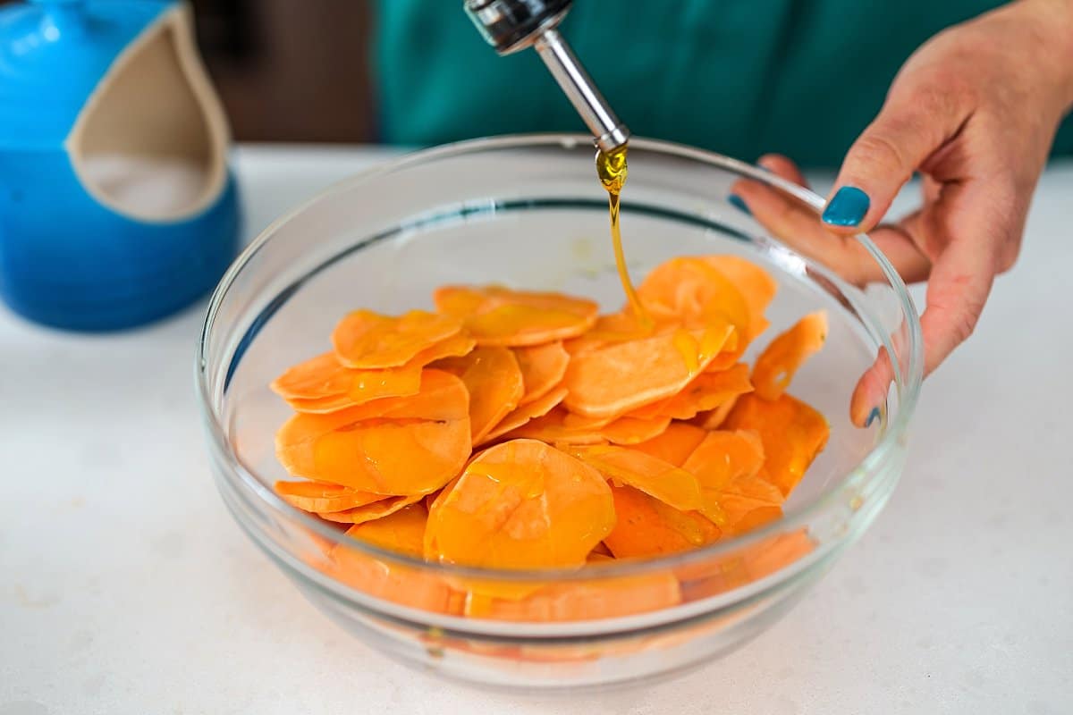 A person holding a glass bowl with sweet potatoes inside
