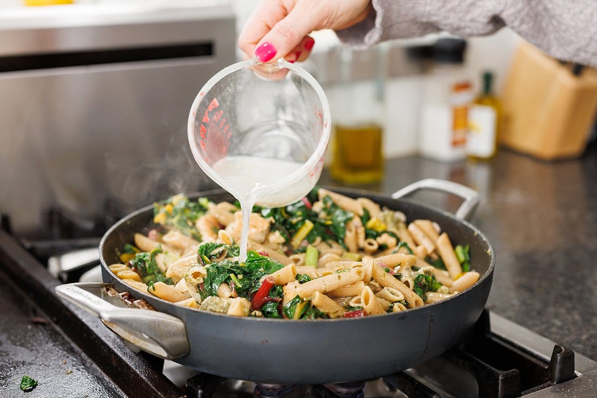 Pouring reserved pasta water to pan with pasta and veggies.