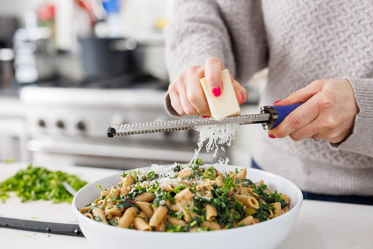 Freshly grating parmesan cheese over pesto chicken pasta with swiss chard.