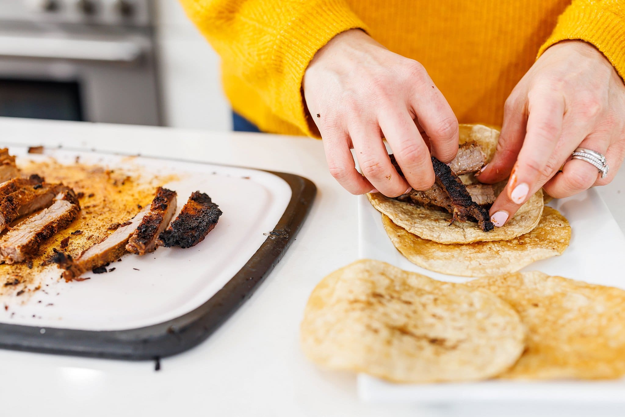 Assembling flank steak tacos on corn tortillas.