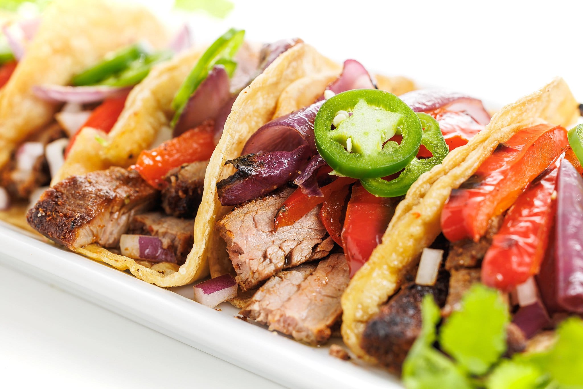 Flank steak tacos topped with grilled veggies and fresh jalapeños.