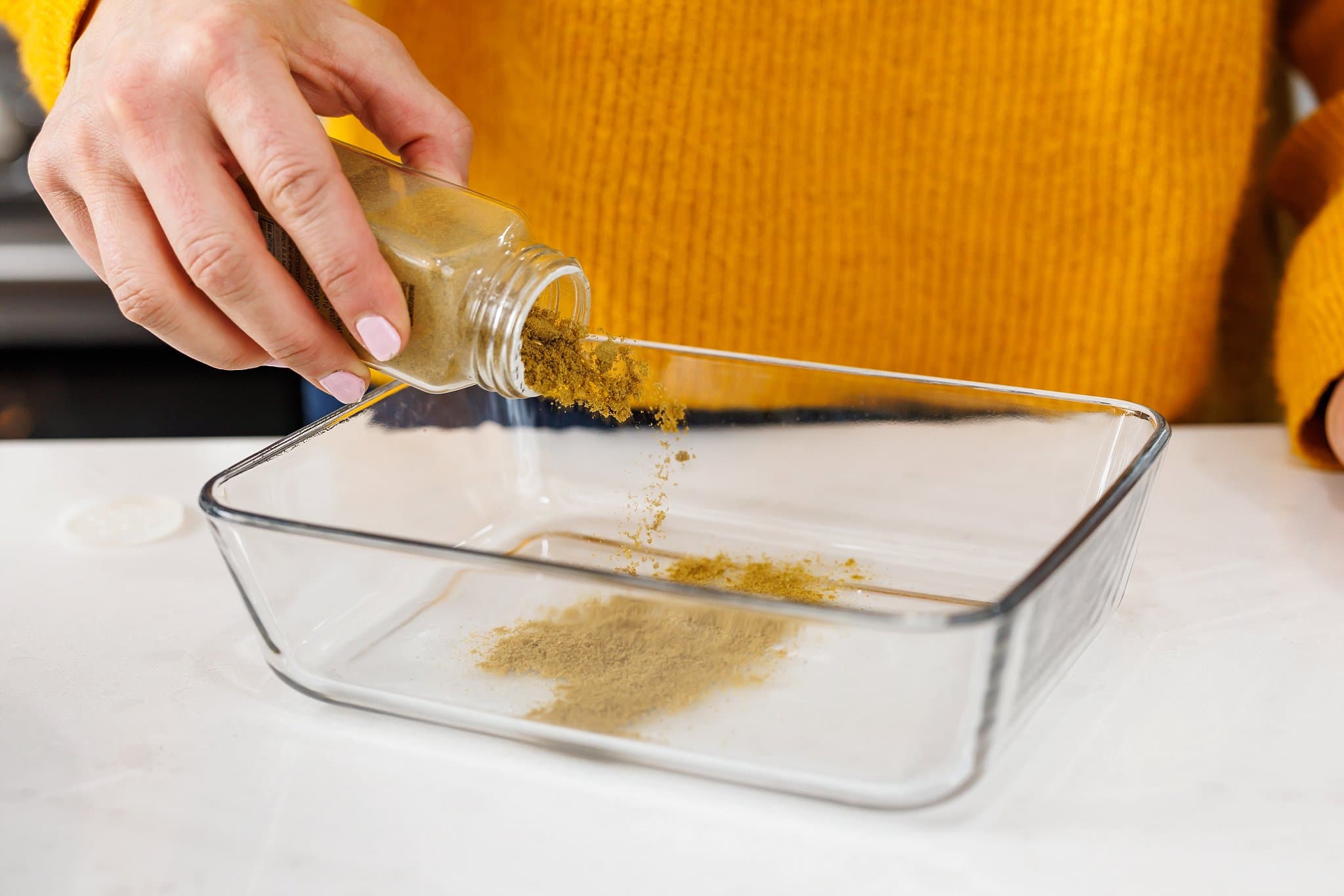 Liz adding cumin to large glass dish.