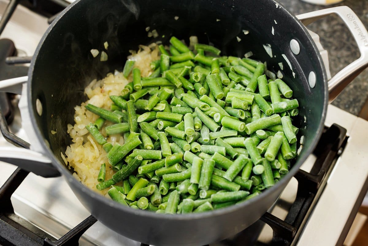 Adding frozen green beans to a pot.