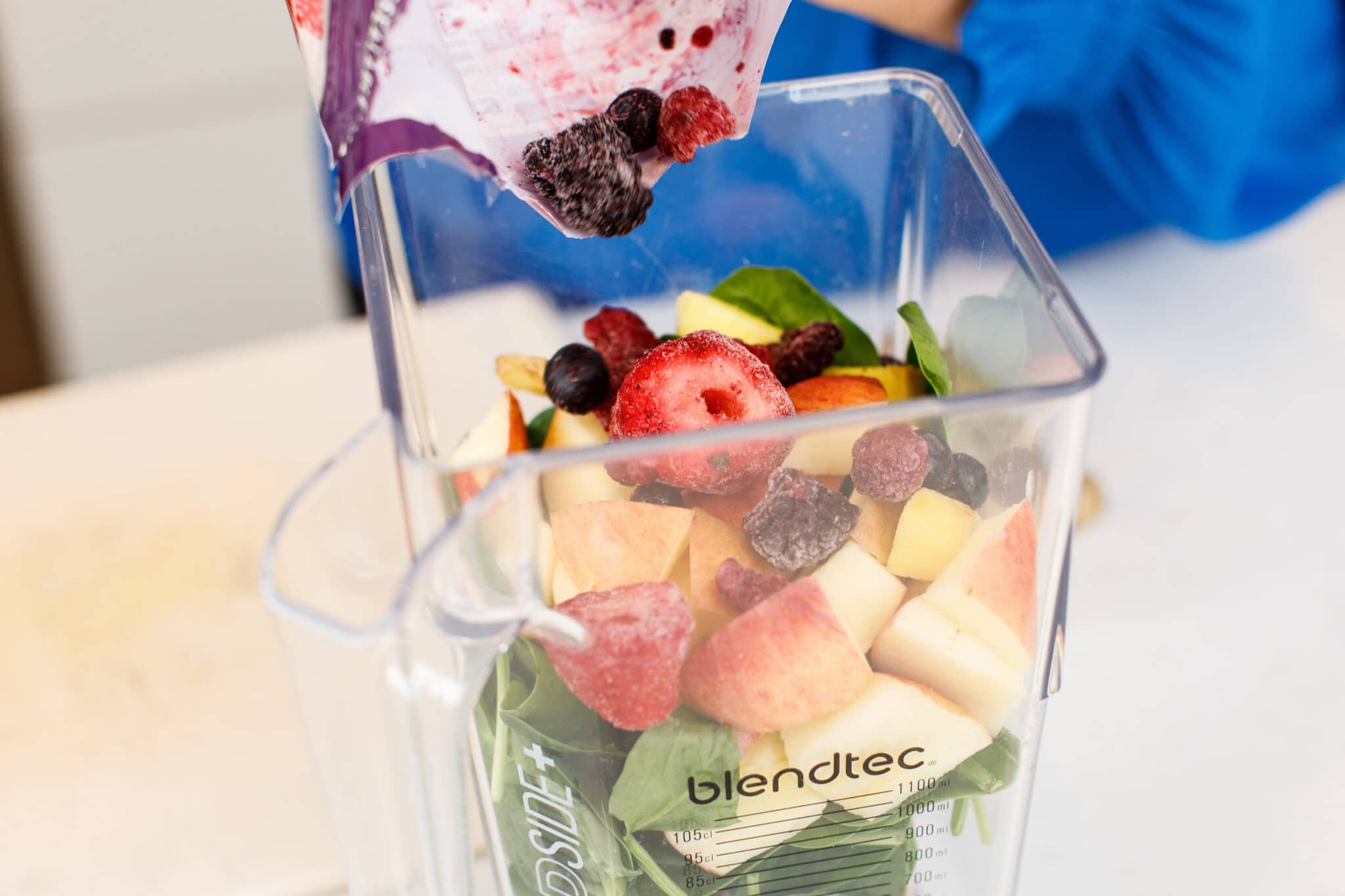 Adding frozen berries to blender with apple and spinach.