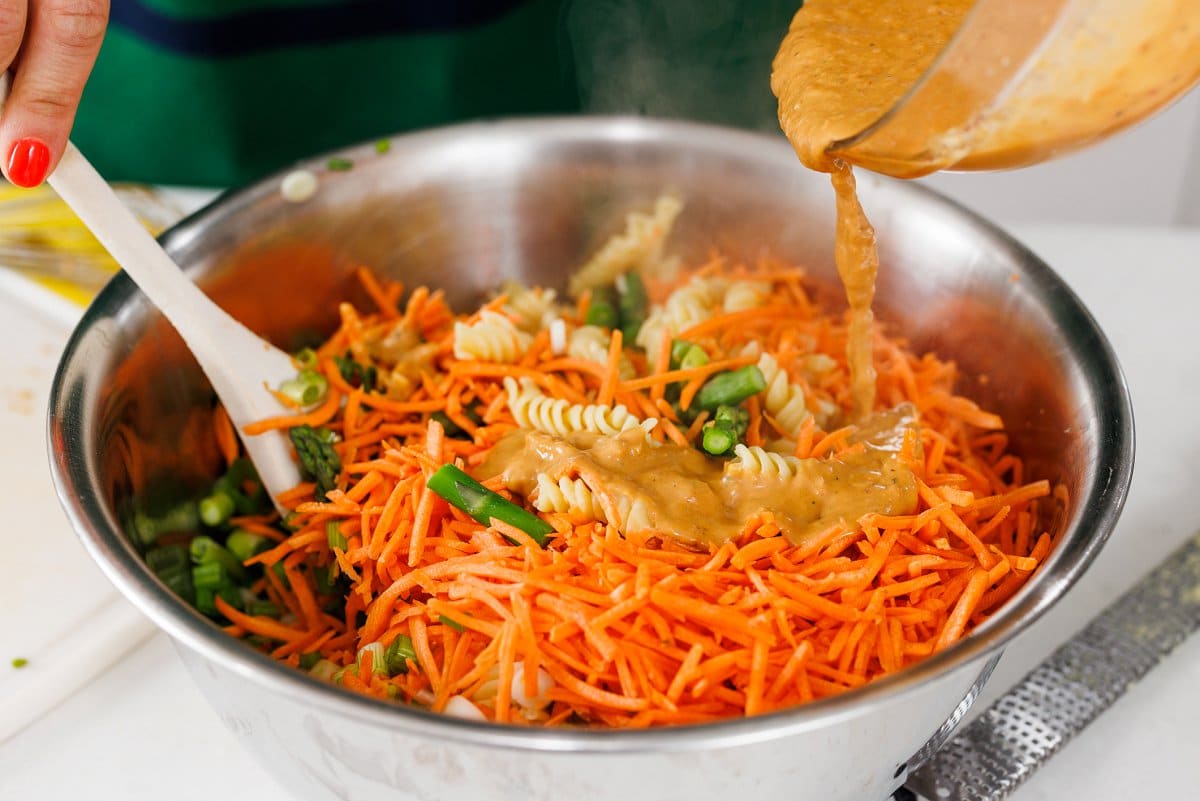 Drizzling peanut dressing over pasta salad.