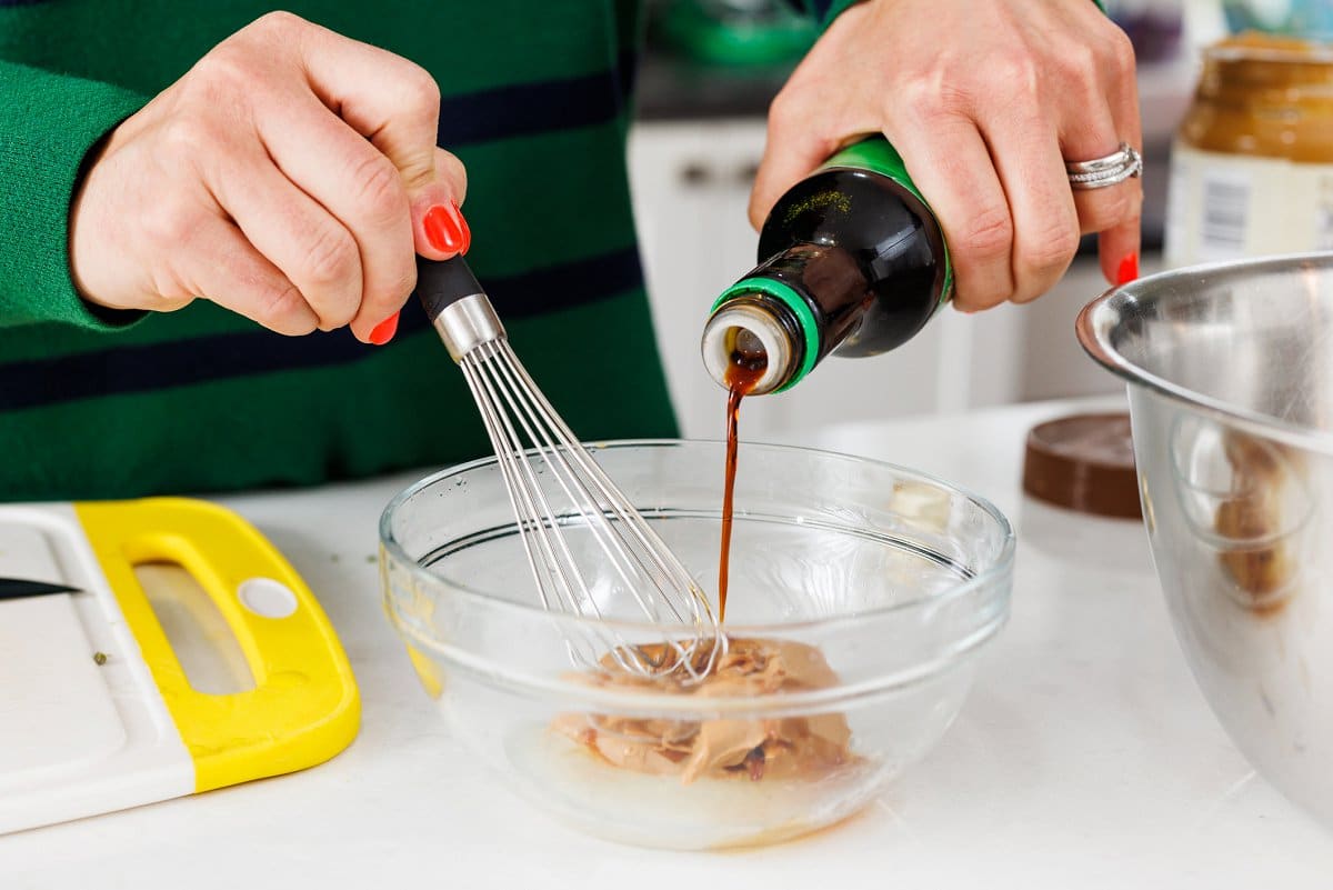 Adding soy sauce to peanut butter in a bowl.