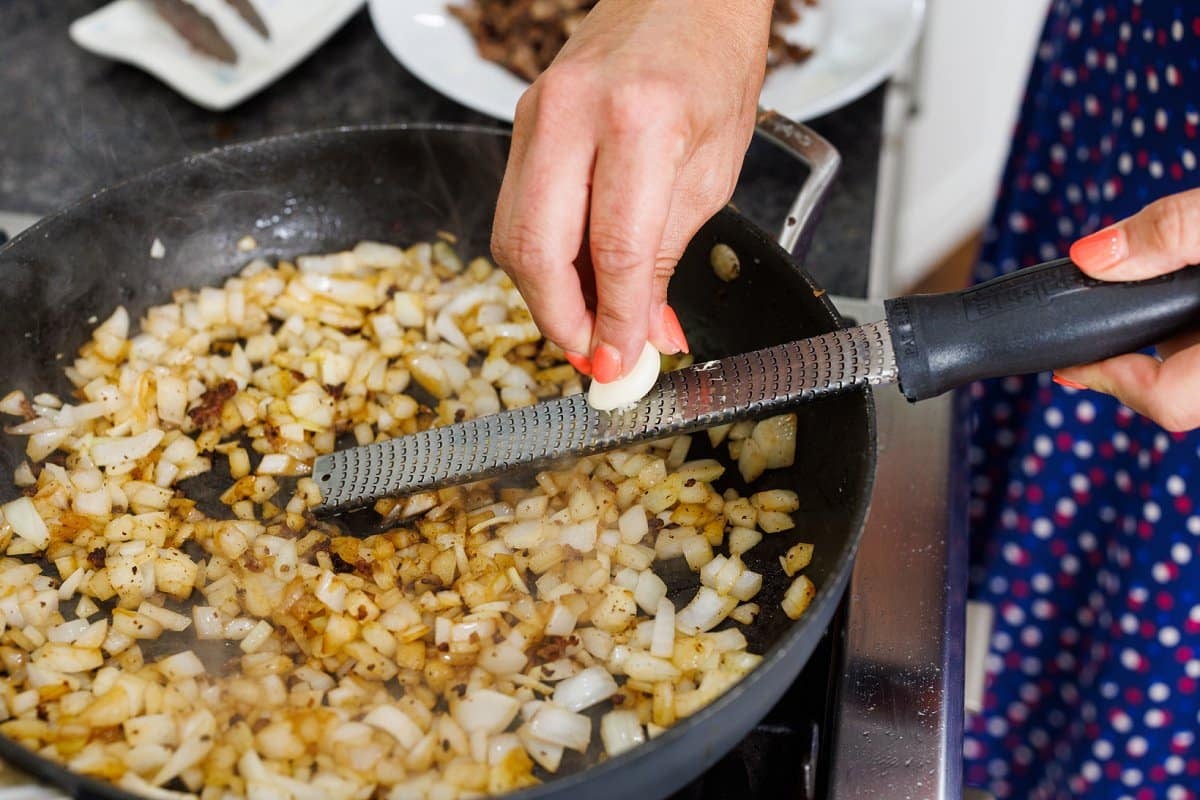 Using a microplane to grate fresh garlic into skillet with onion.
