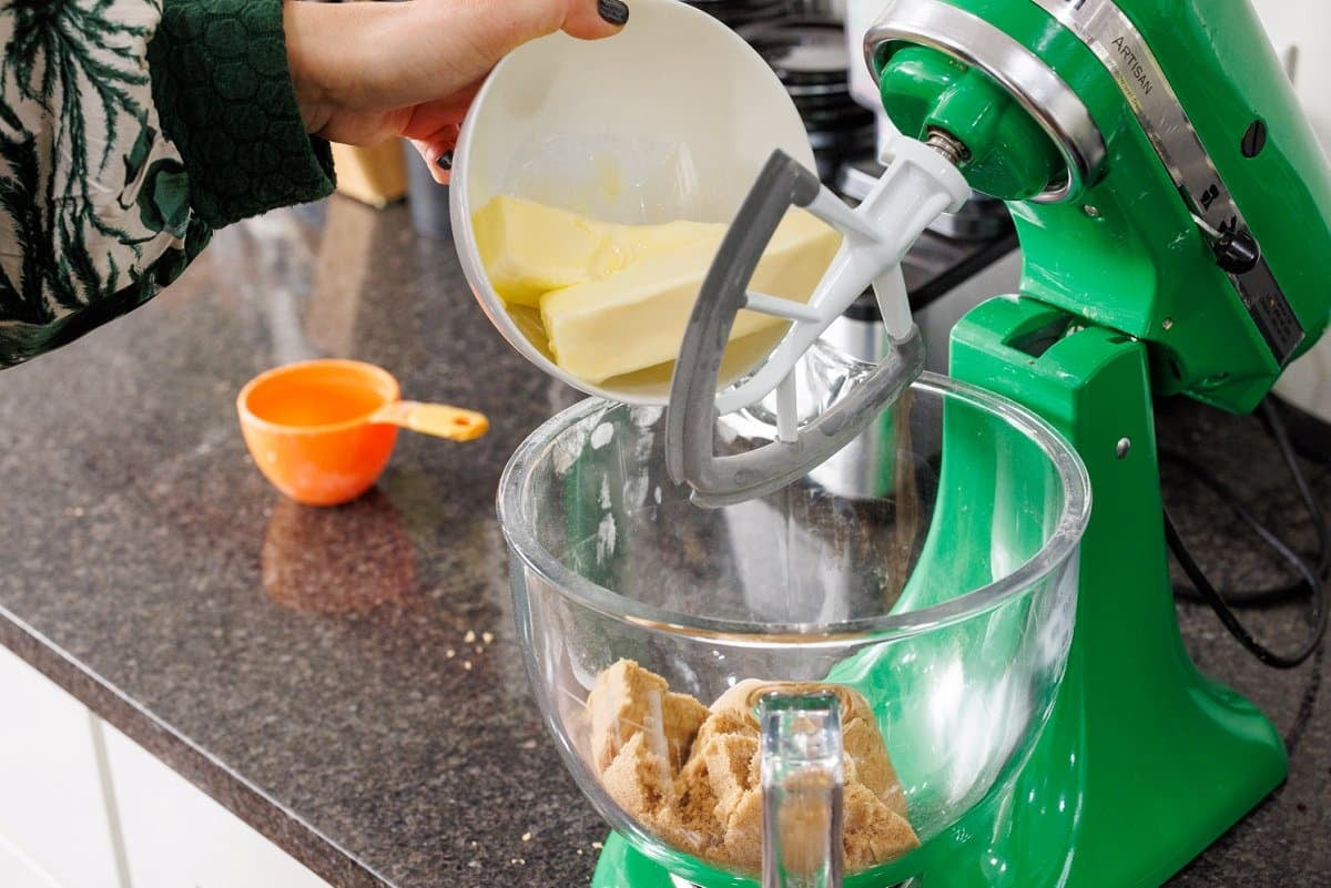 Adding sticks of butter to a glass bowl of a stand mixer.