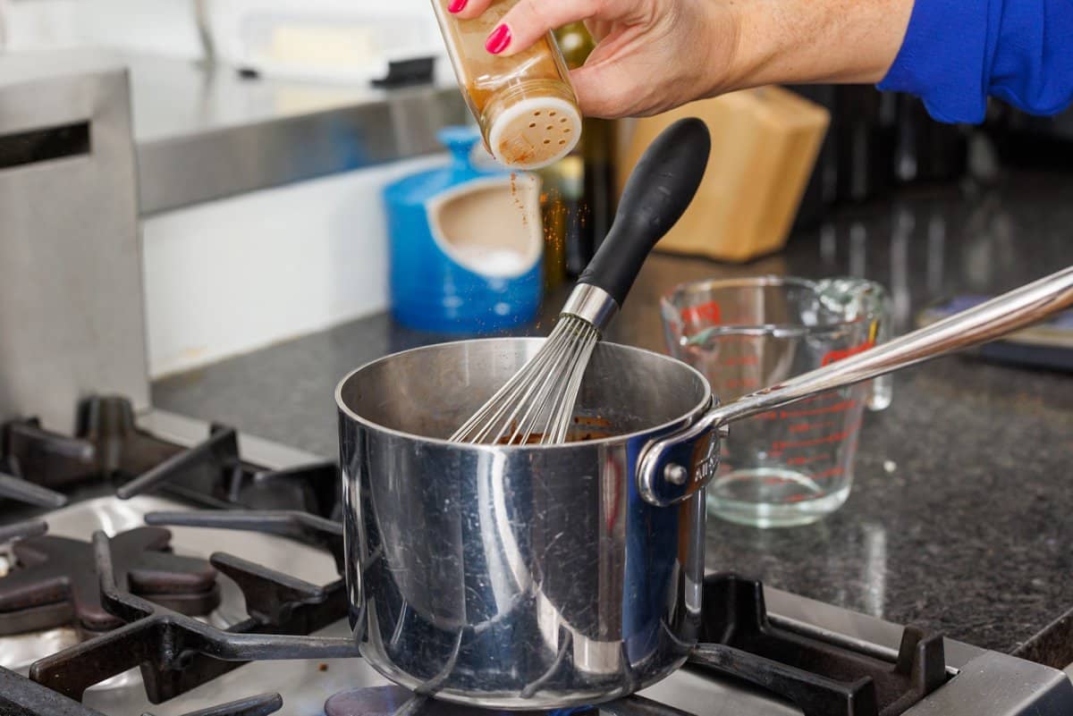 Sprinkling cayenne pepper powder into sauce pan.