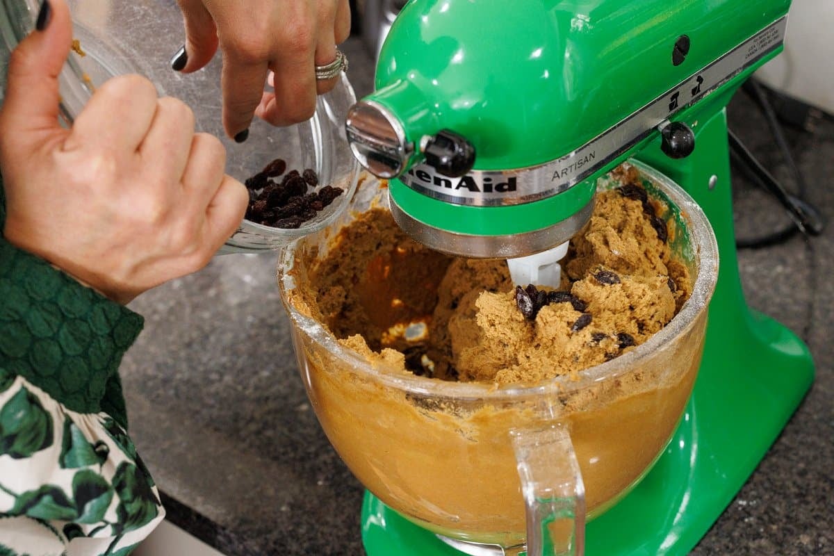 Slowly adding raisins to cookie dough in stand mixer bowl.