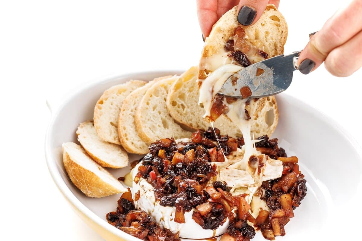 Spreading baked brie with apple cherry compote on a baguette slice.