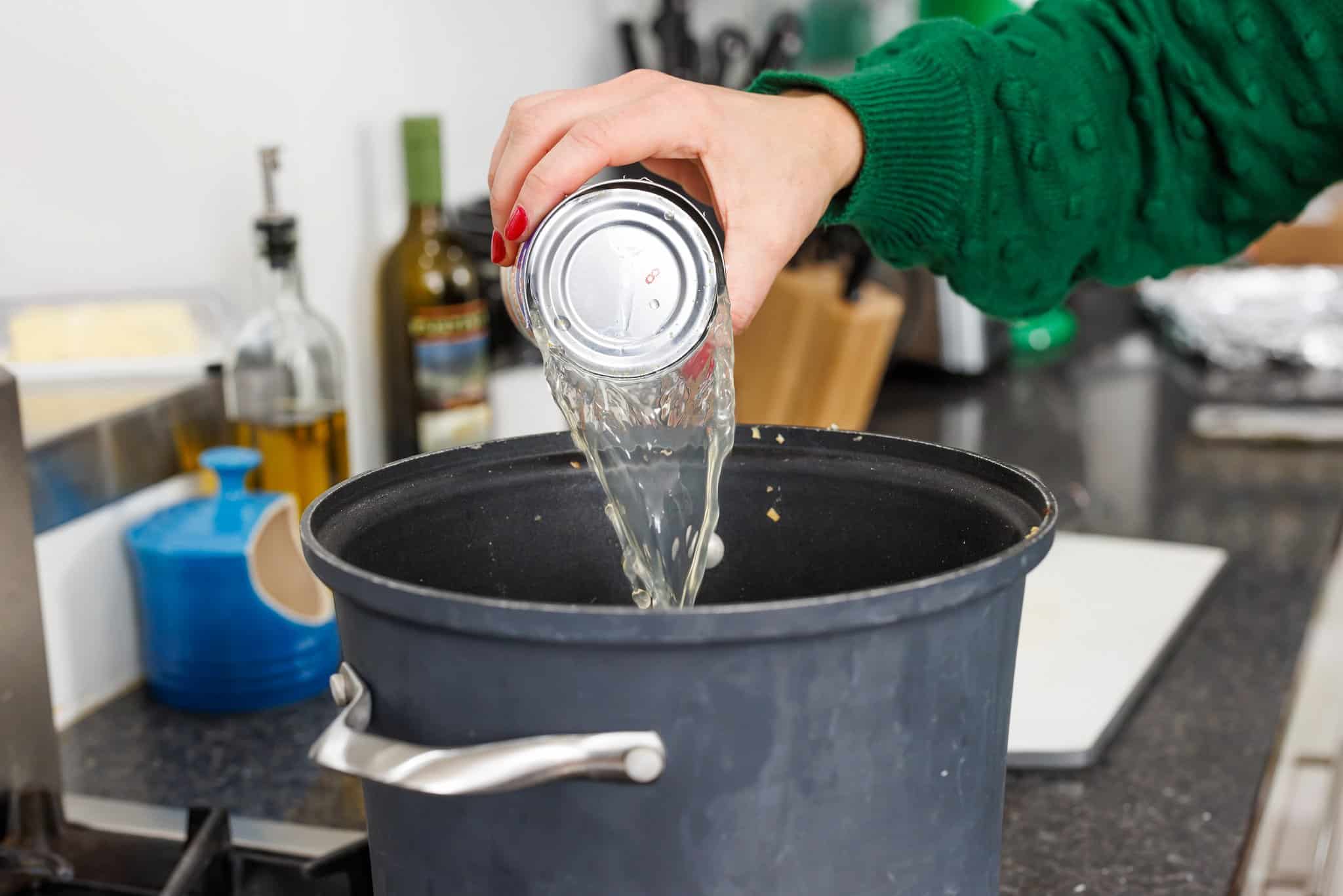 Pouring canned chicken broth into pot.
