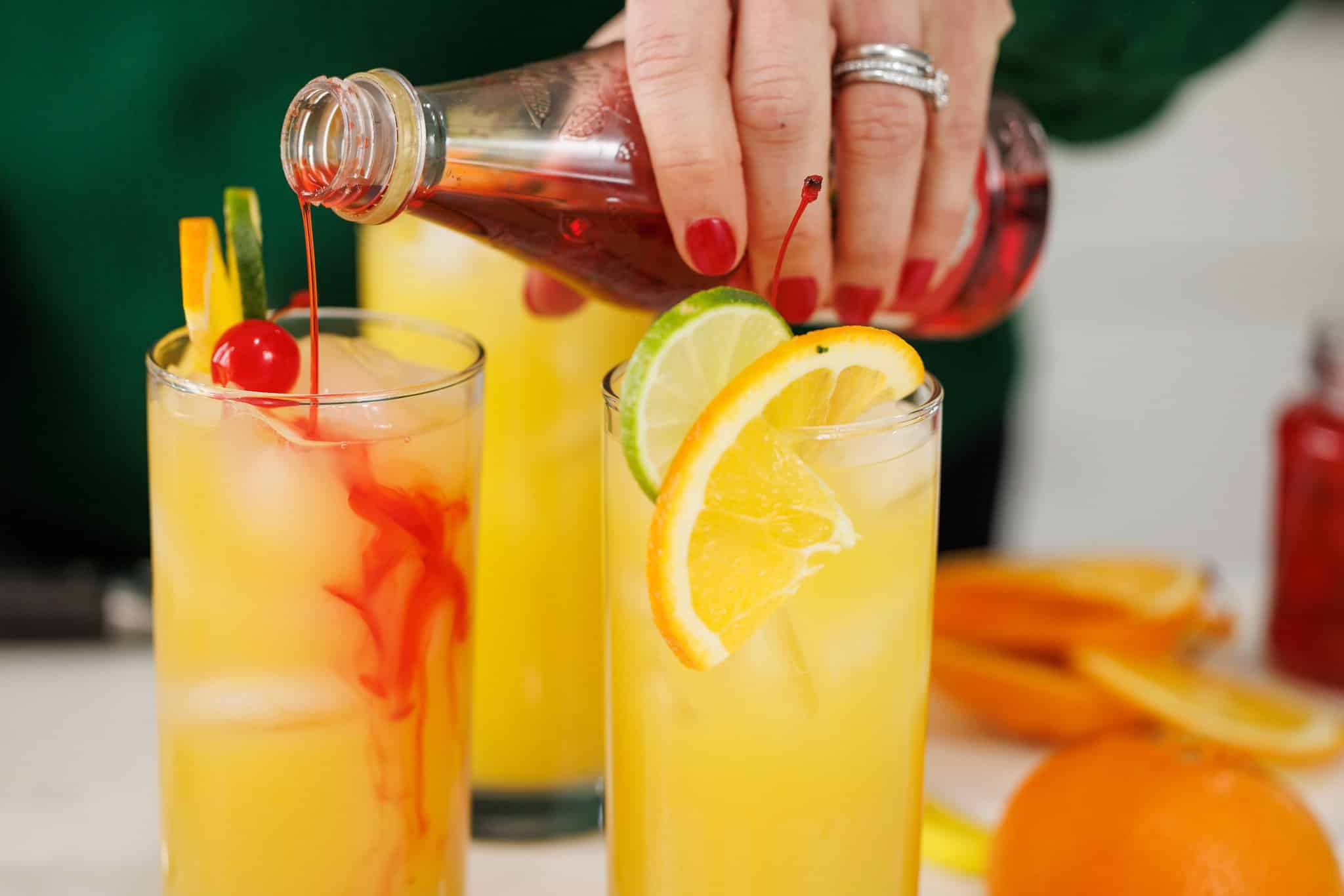 Adding grenadine to glasses of hurricane cocktail.