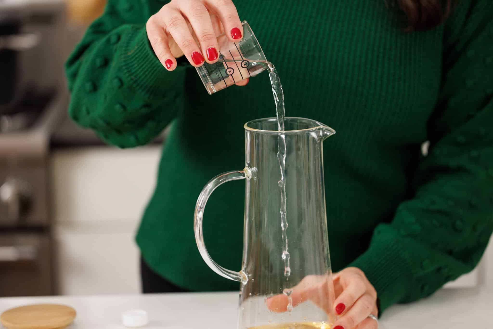 Pouring light rum into glass pitcher.