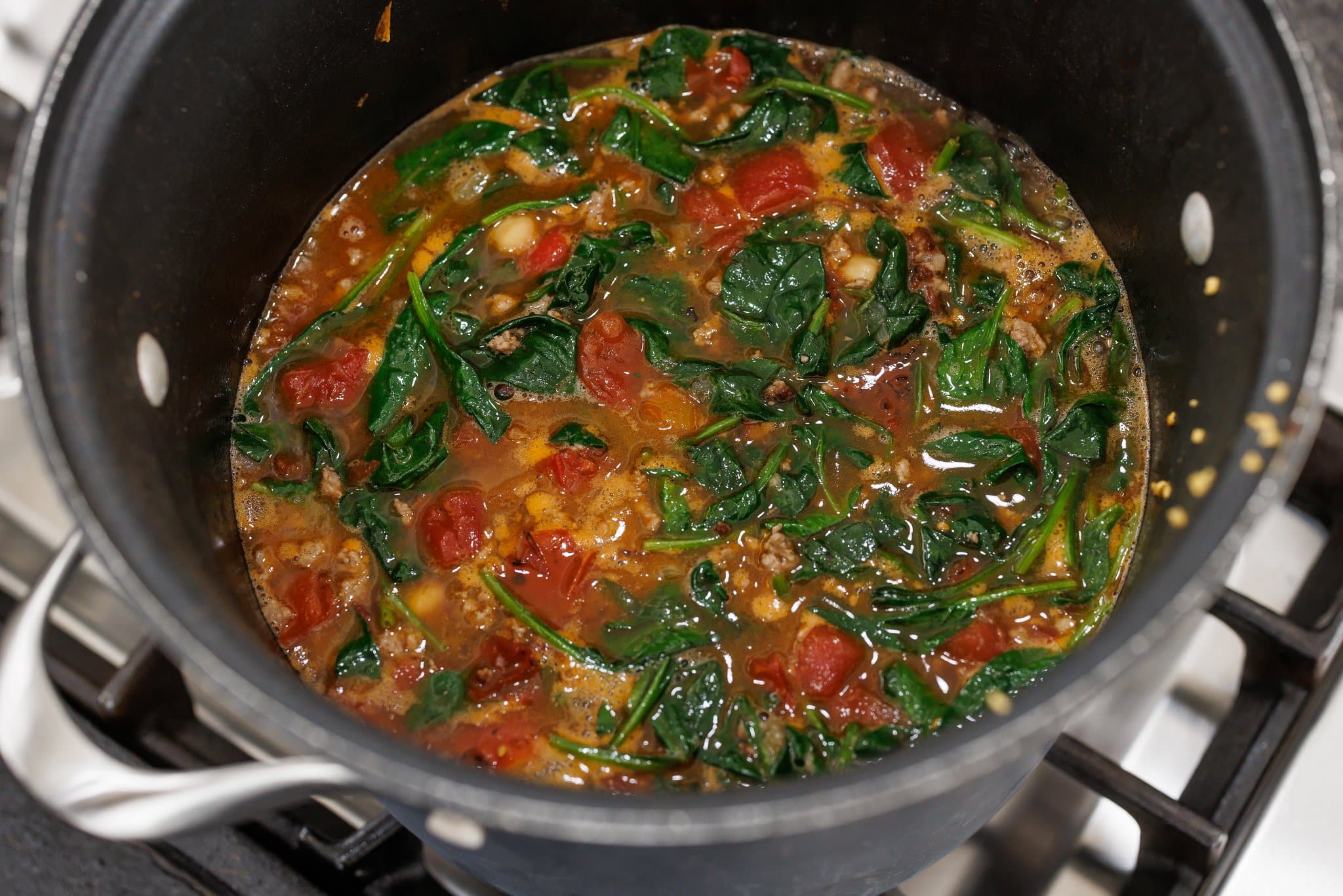 Simmering lamb and chickpeas stew with spinach in large pot on stove.