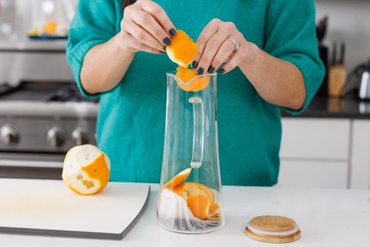 Orange peels being added to glass pitcher.