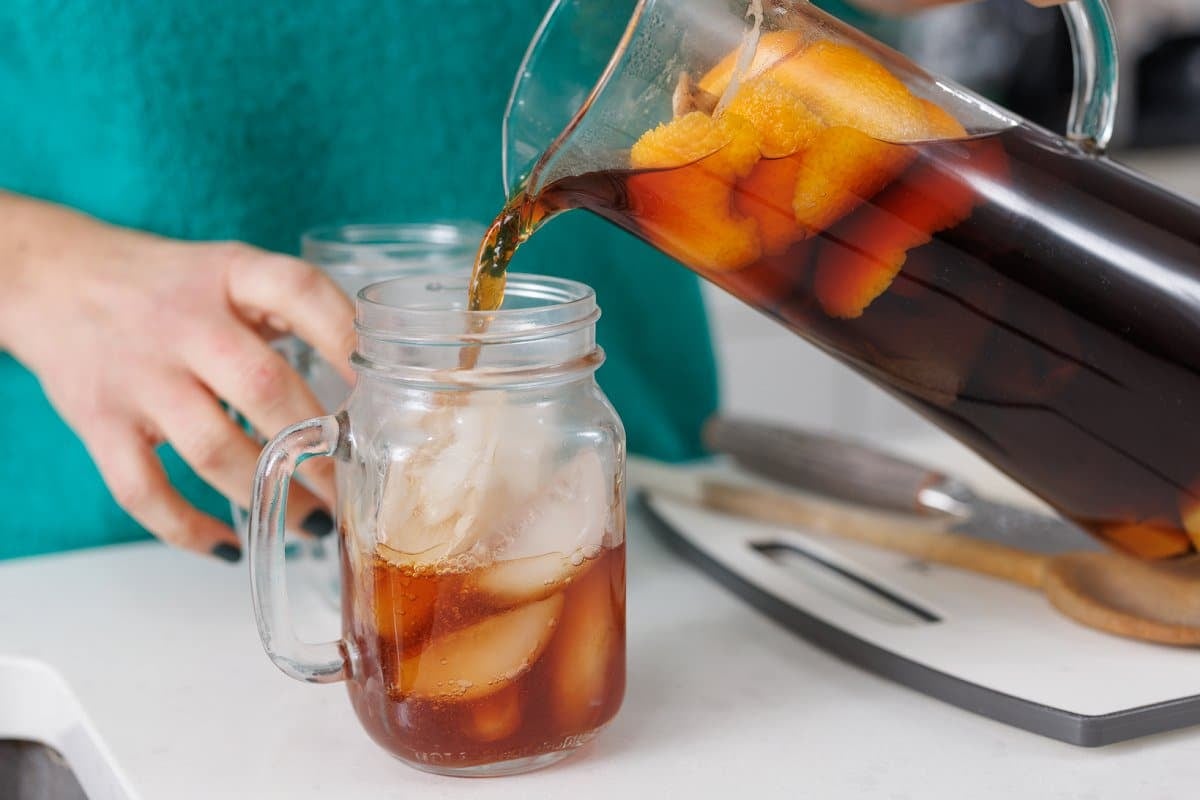 Pouring orange ginger tea into a glass over ice.