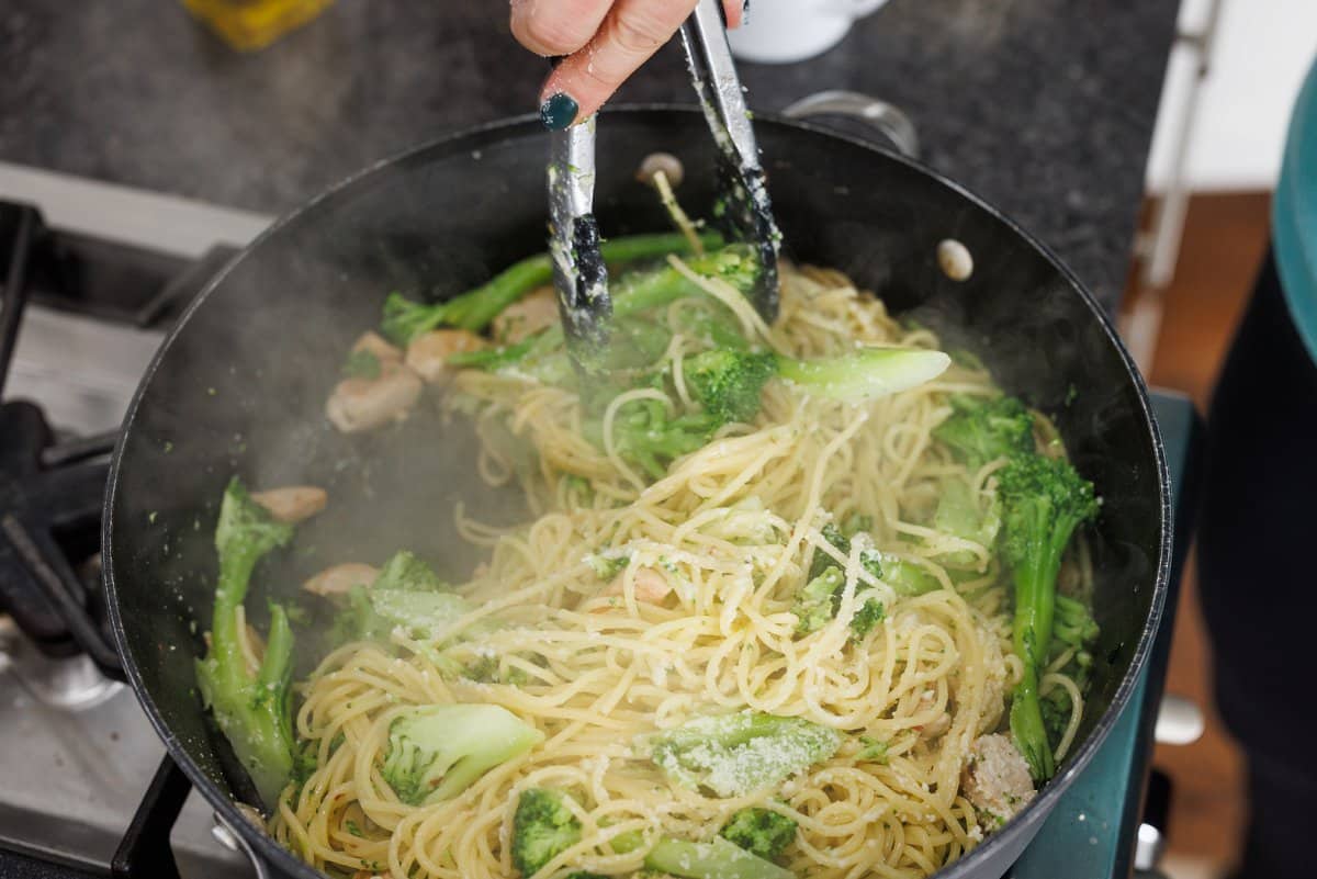 Tossing lemon pasta with chicken and broccoli in skillet.