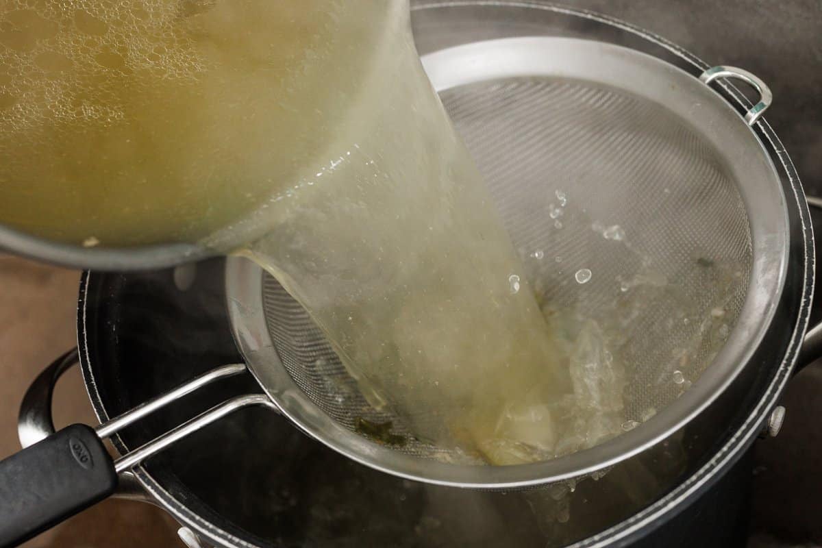 Straining chicken stock into pot.