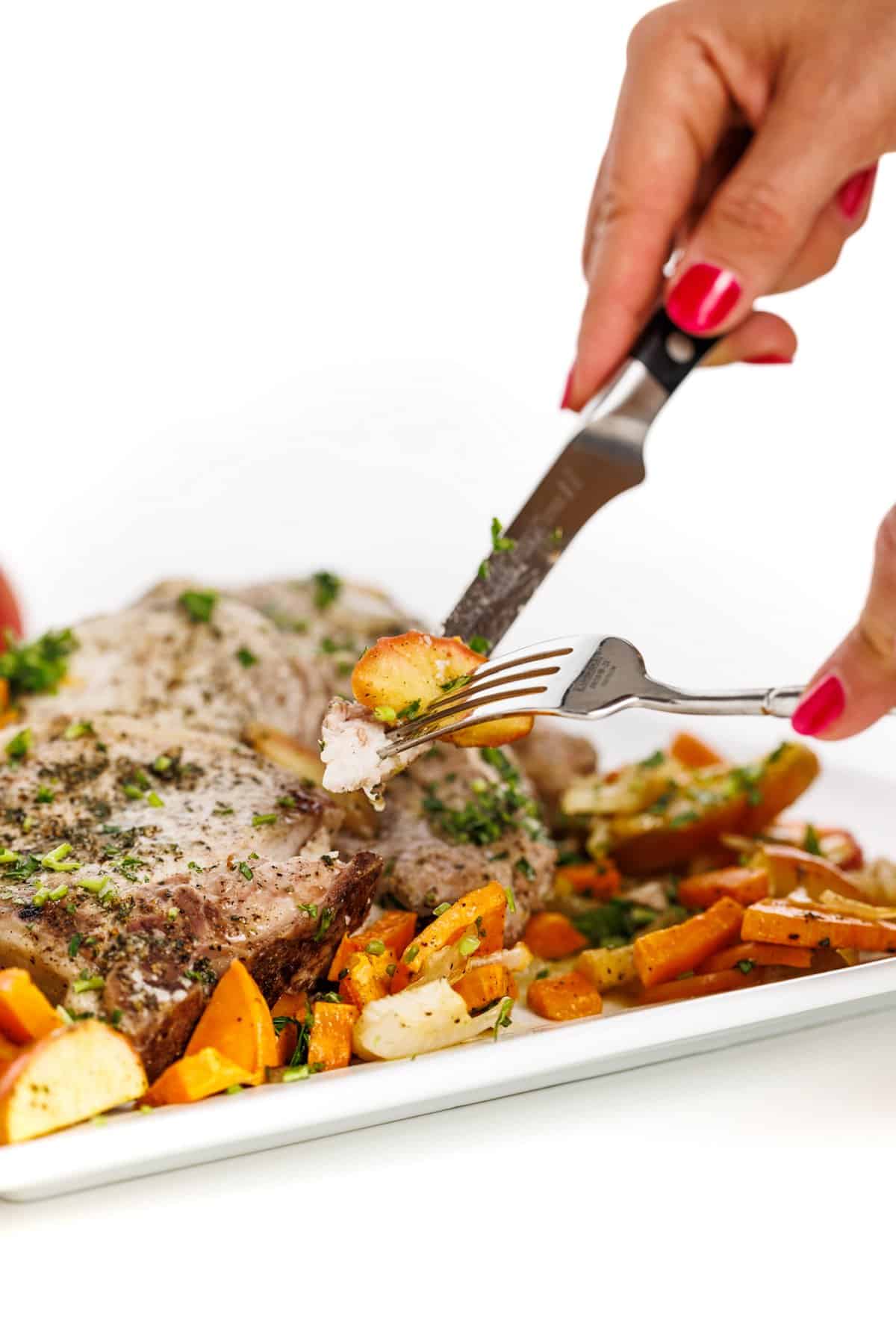 Forkful of sheet pan pork chops with apples, onions, and sweet potatoes.