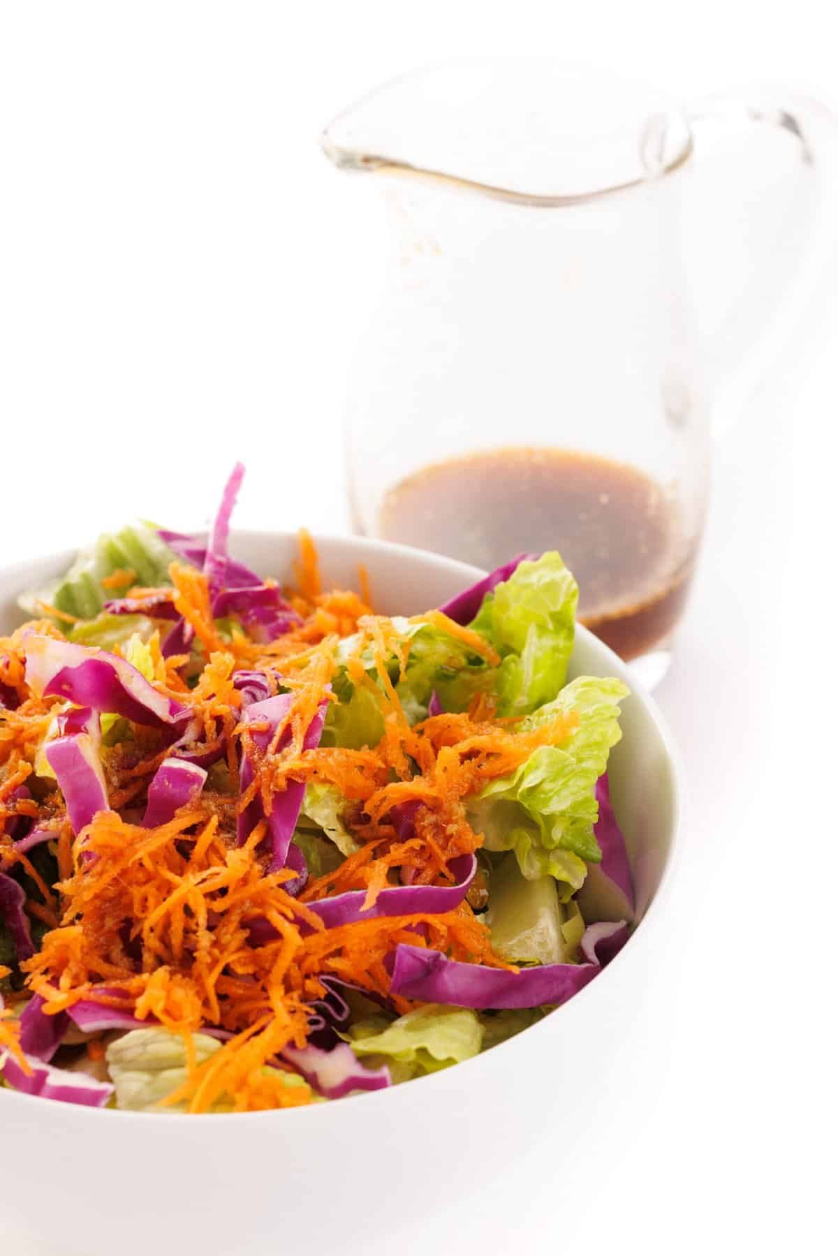 Ginger salad dressing in a pitcher next to a bowl of salad.