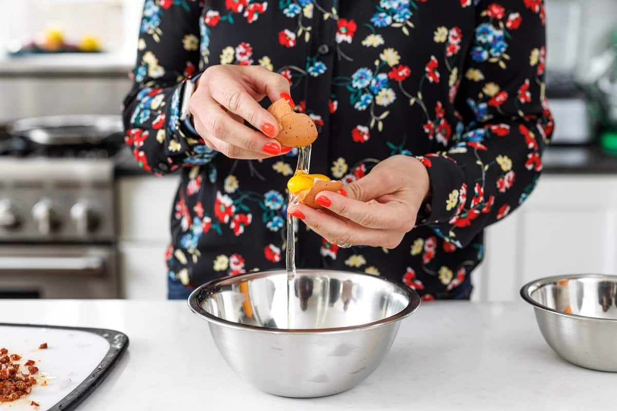 Liz using an egg shell to separate yolk from the whites into a bowl.