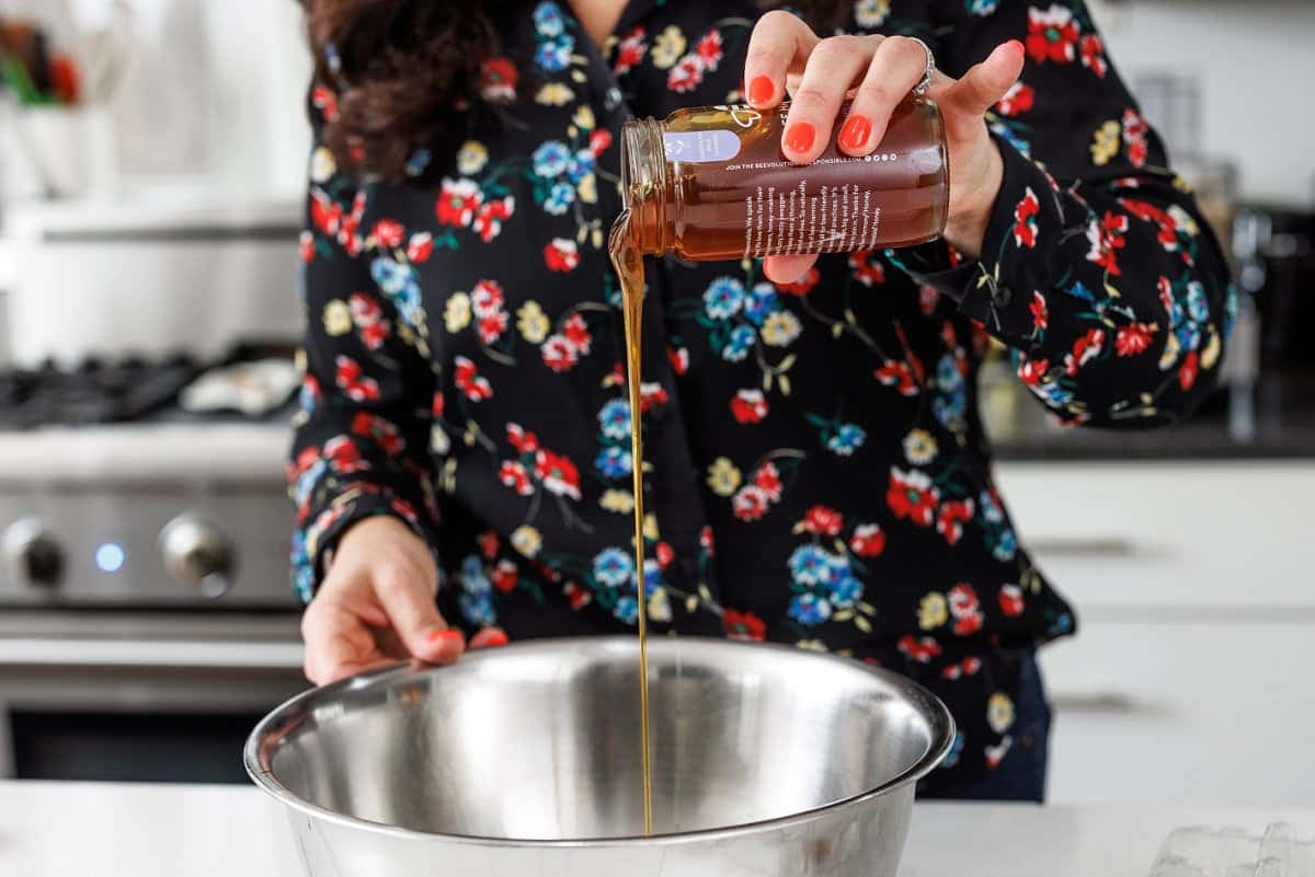 Liz adding honey to a large metal bowl.