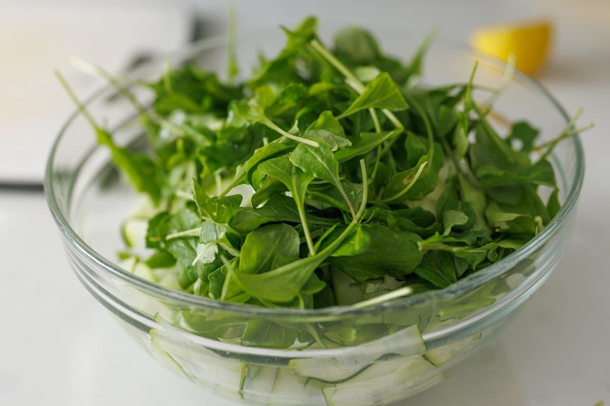 Arugula added to a large glass bowl.