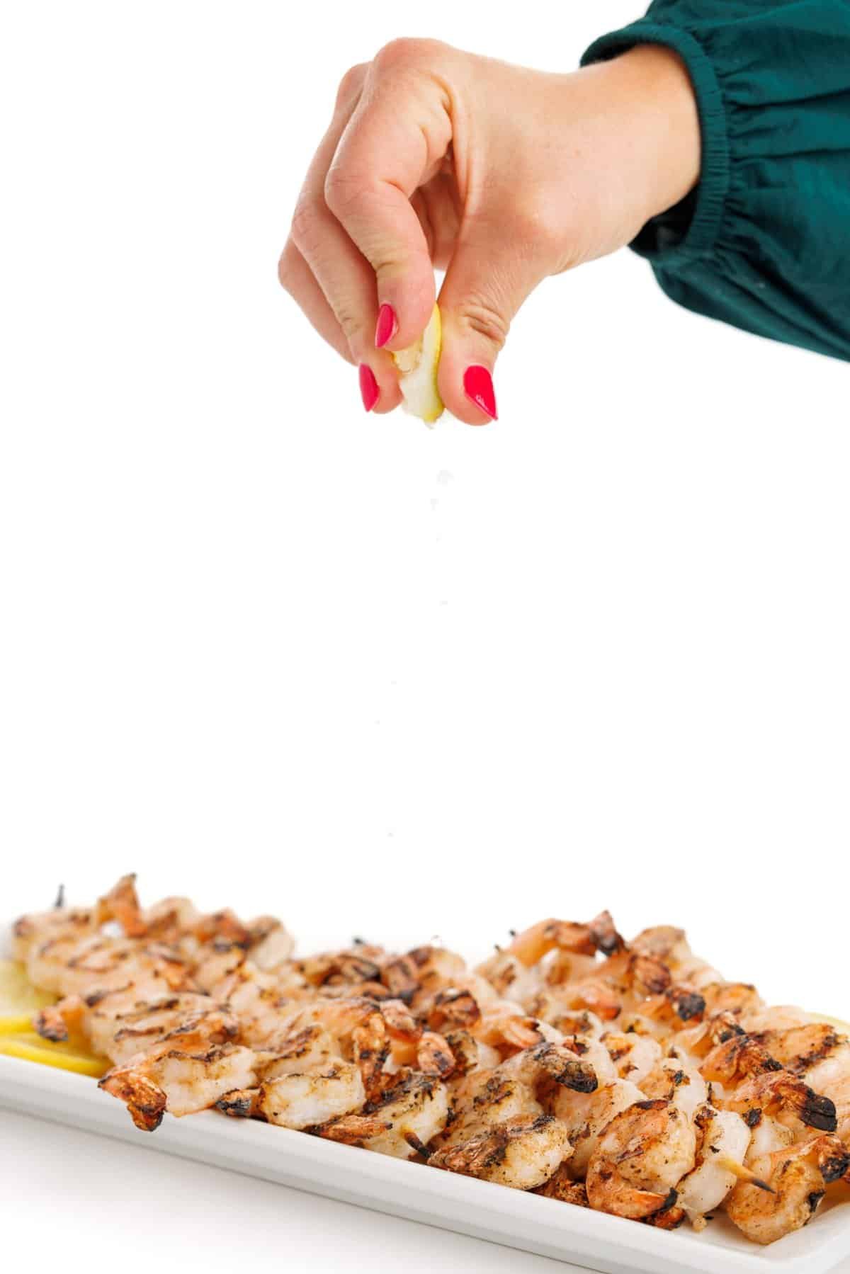 Garnishing grilled shrimp shawarma skewers with lemon juice.