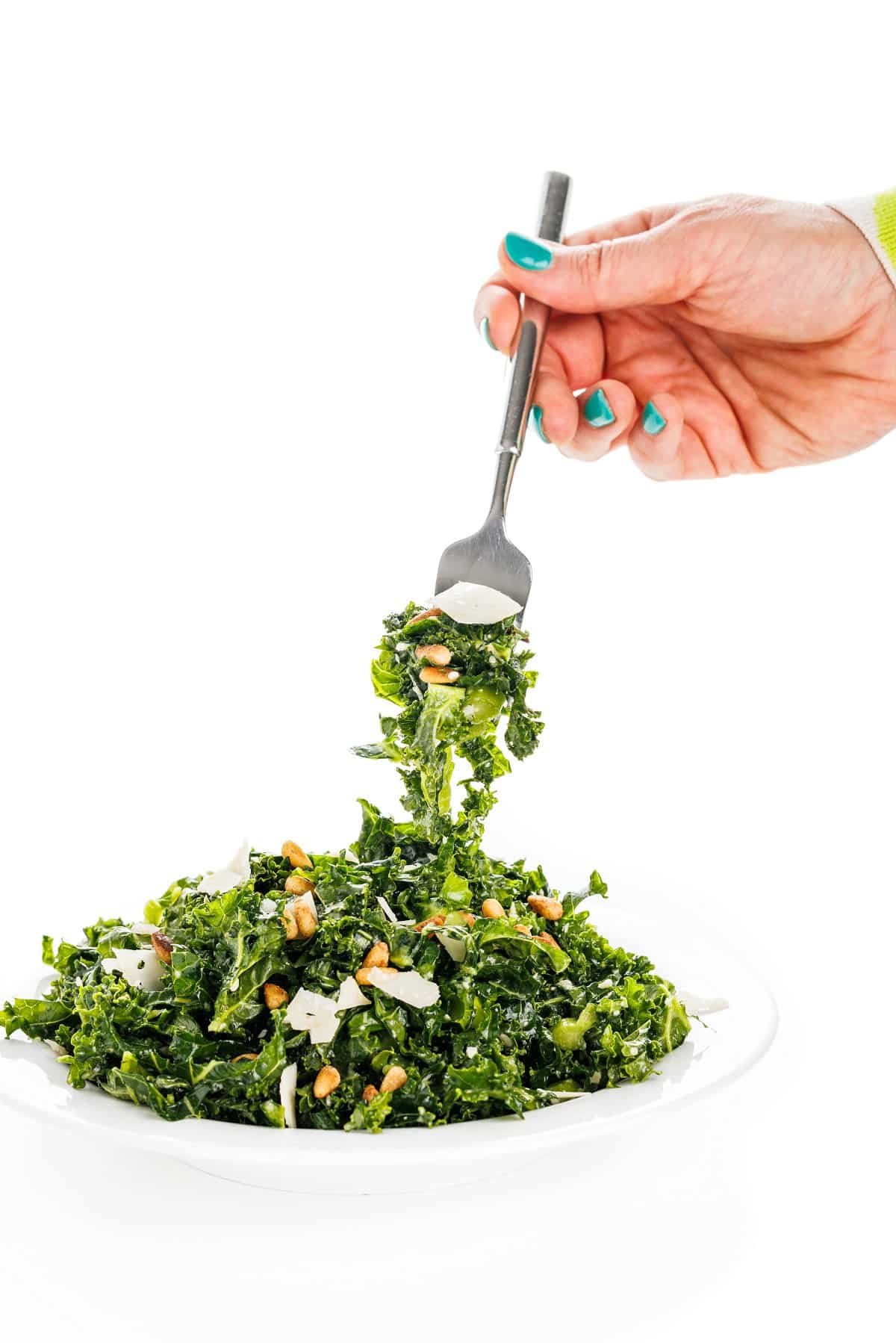 Forkful of kale Caesar salad on a white plate.
