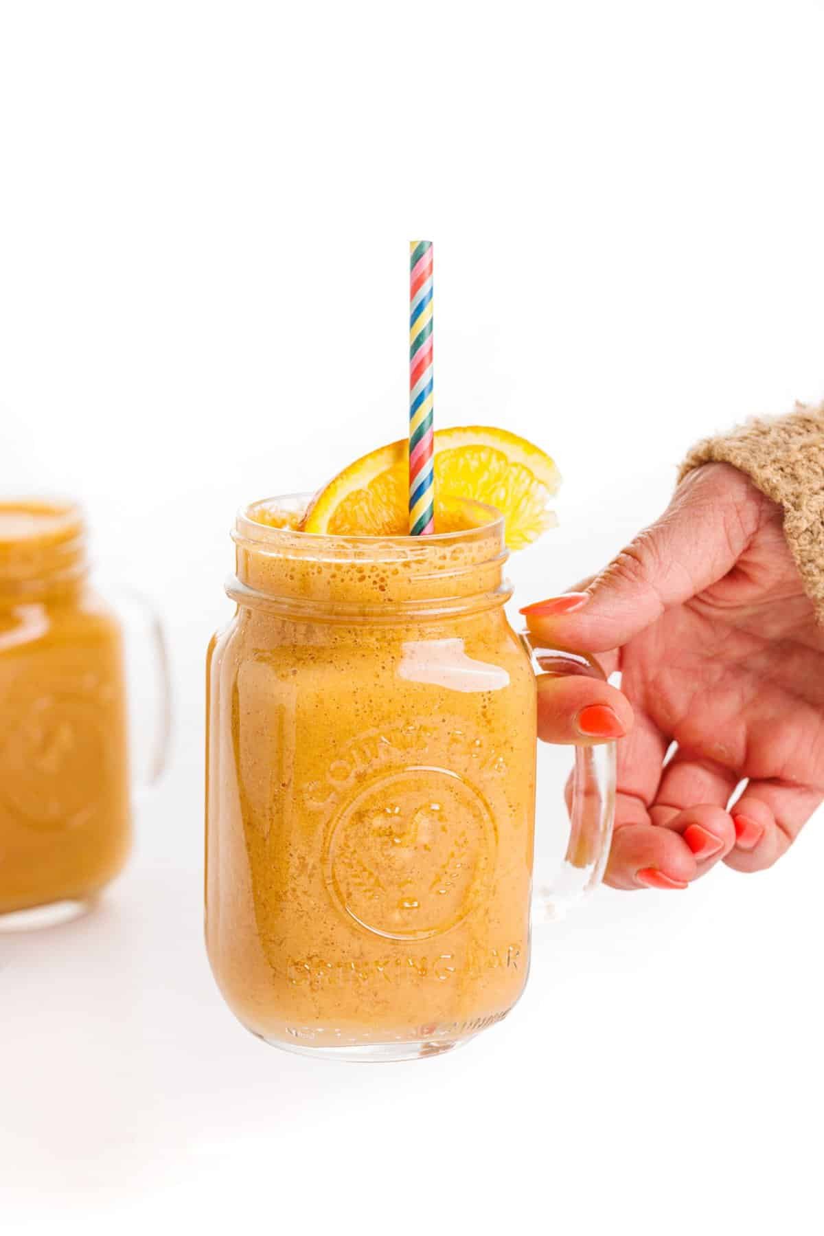 Holding an orange ginger detox smoothie.