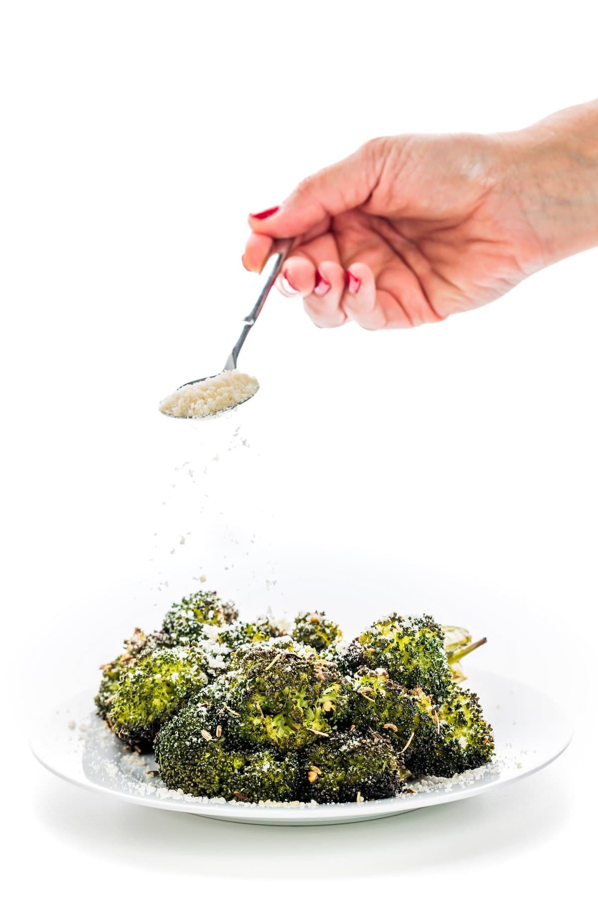 Garnishing Italian herb roasted broccoli with parmesan cheese.