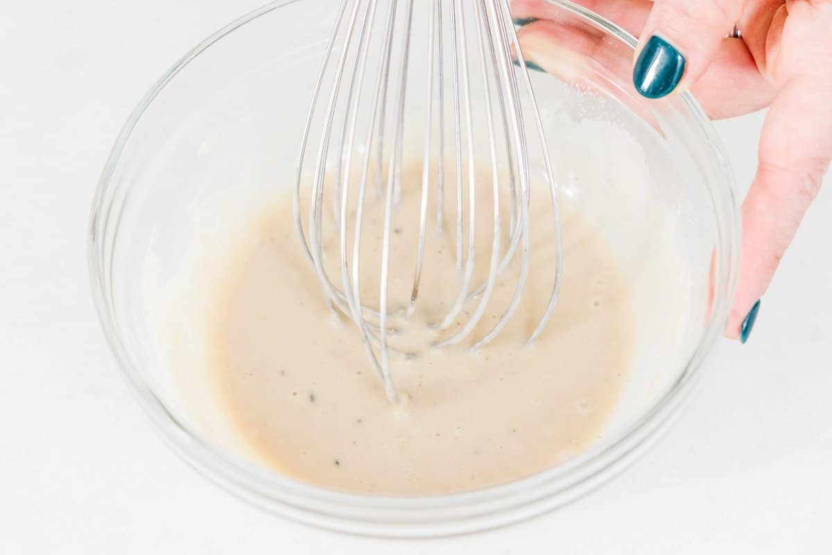 Whisking tahini lemon sauce in glass bowl.