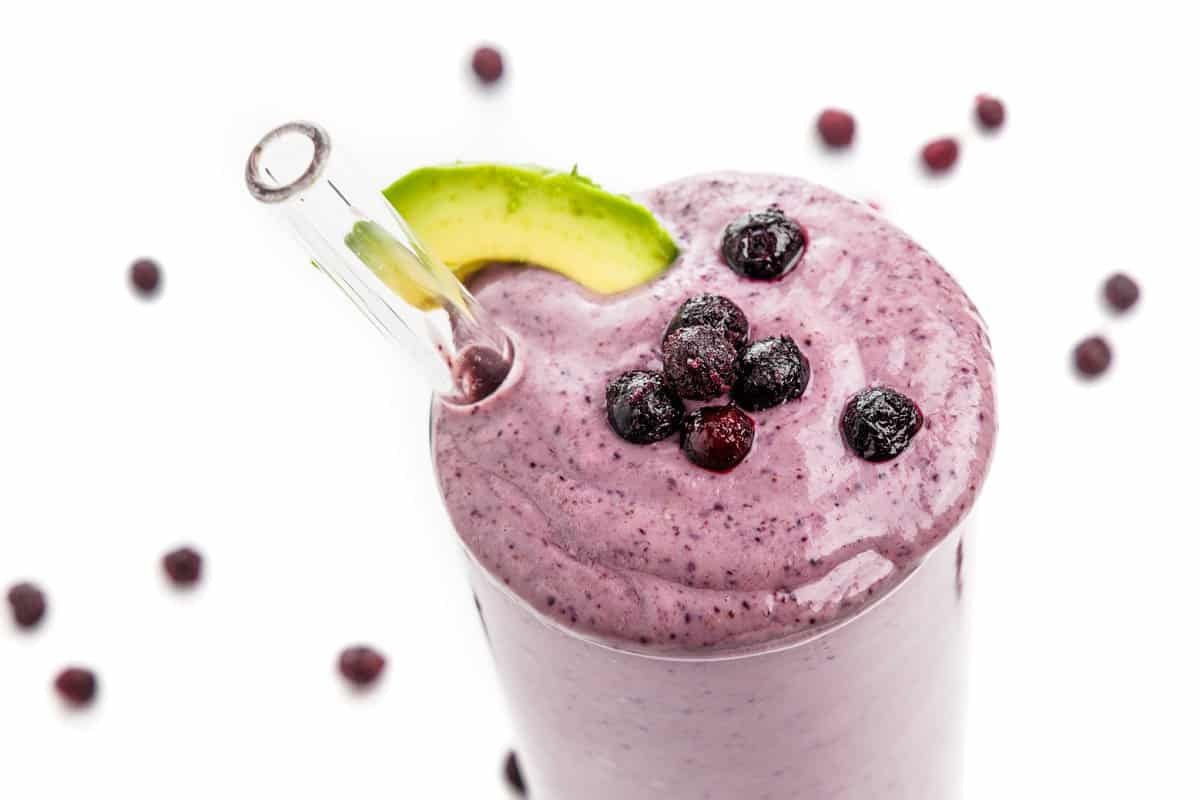 Avocado blueberry smoothie with a slice of avocado, a few blueberries, and a clear smoothie straw.
