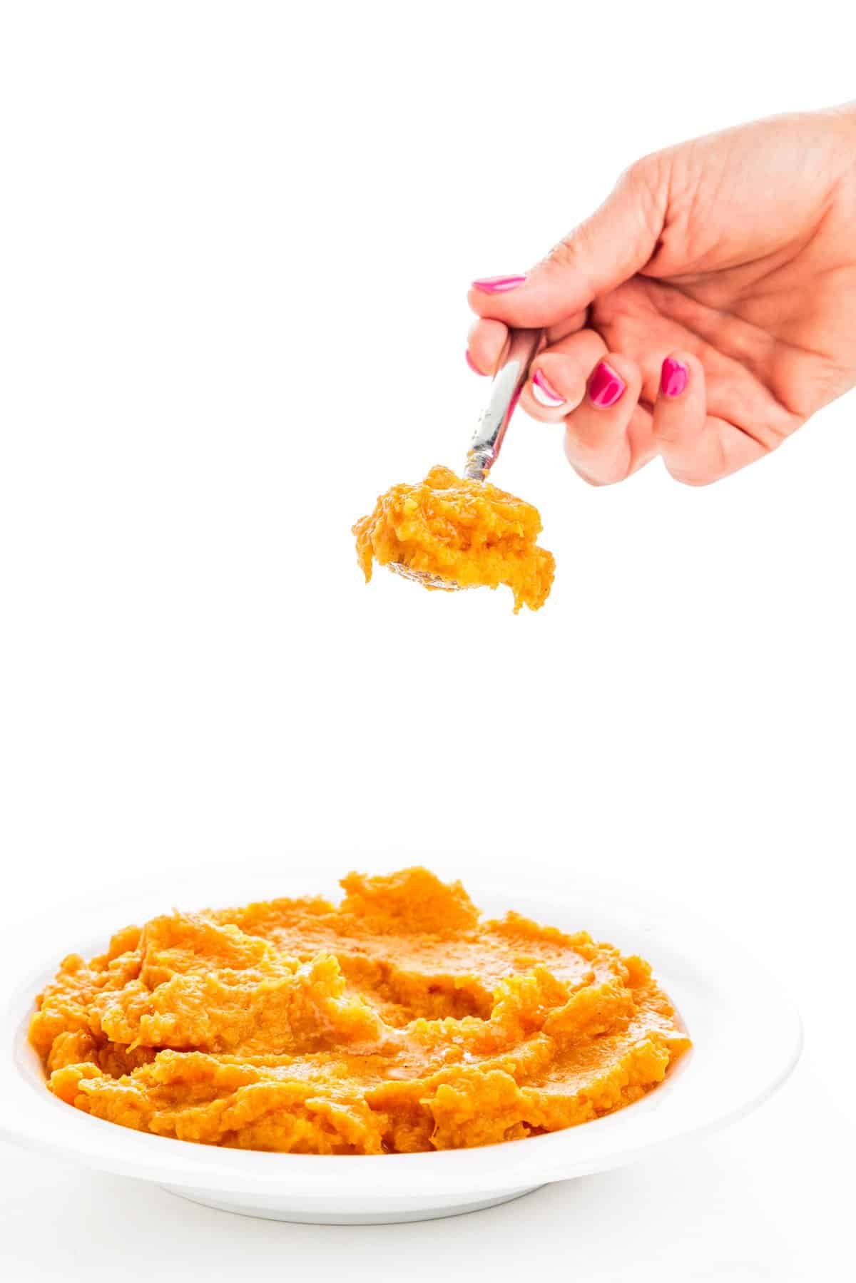 Spoonful of mashed butternut squash and sweet potatoes over a shallow bowl.