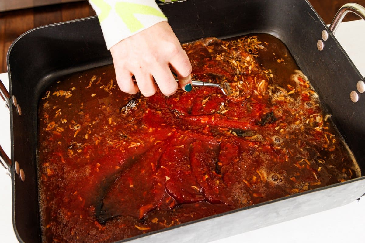 Mixing together sauce for brisket in the bottom of a roasting pan.