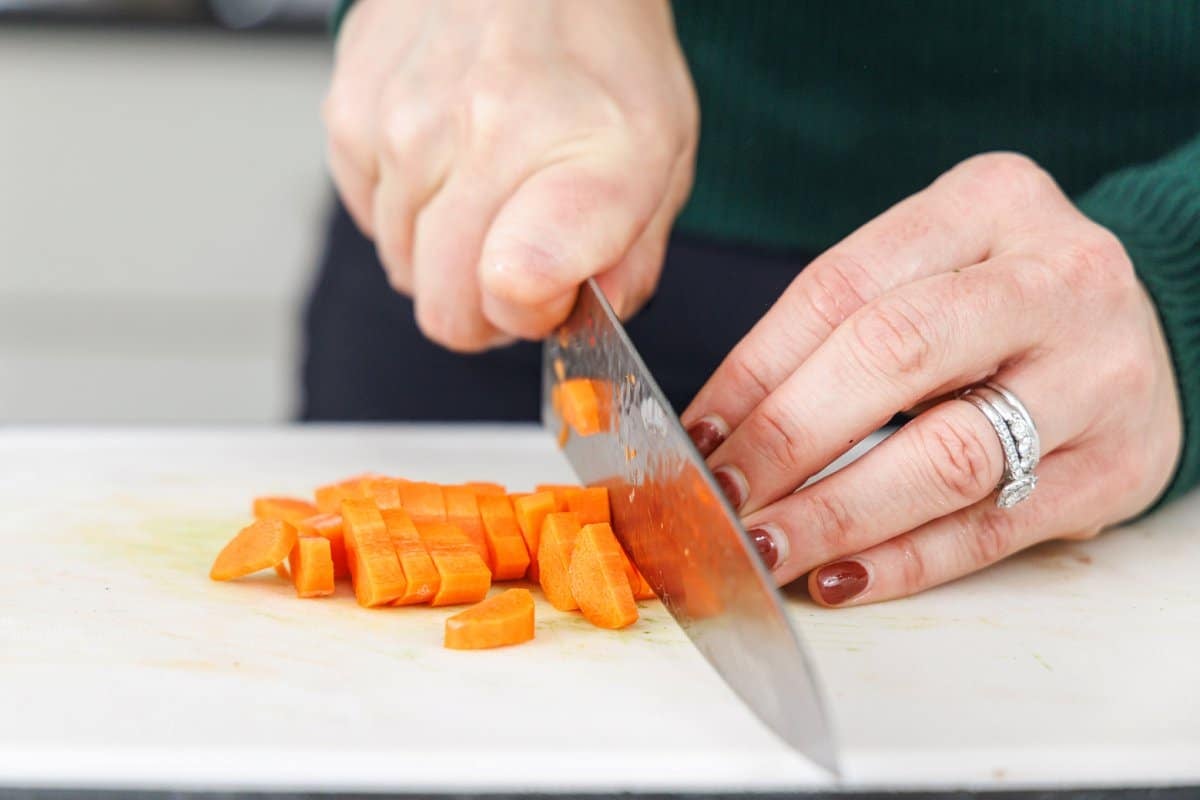Chopping a carrot into small pieces with a large, sharp knife.