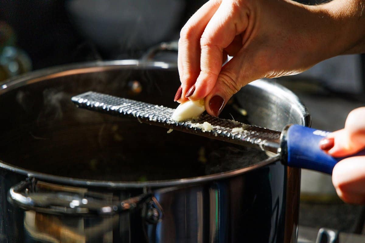 Grating garlic into a large pot on the stove.