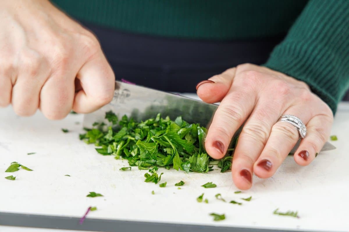 Mincing fresh parsley with a large, sharp knife.