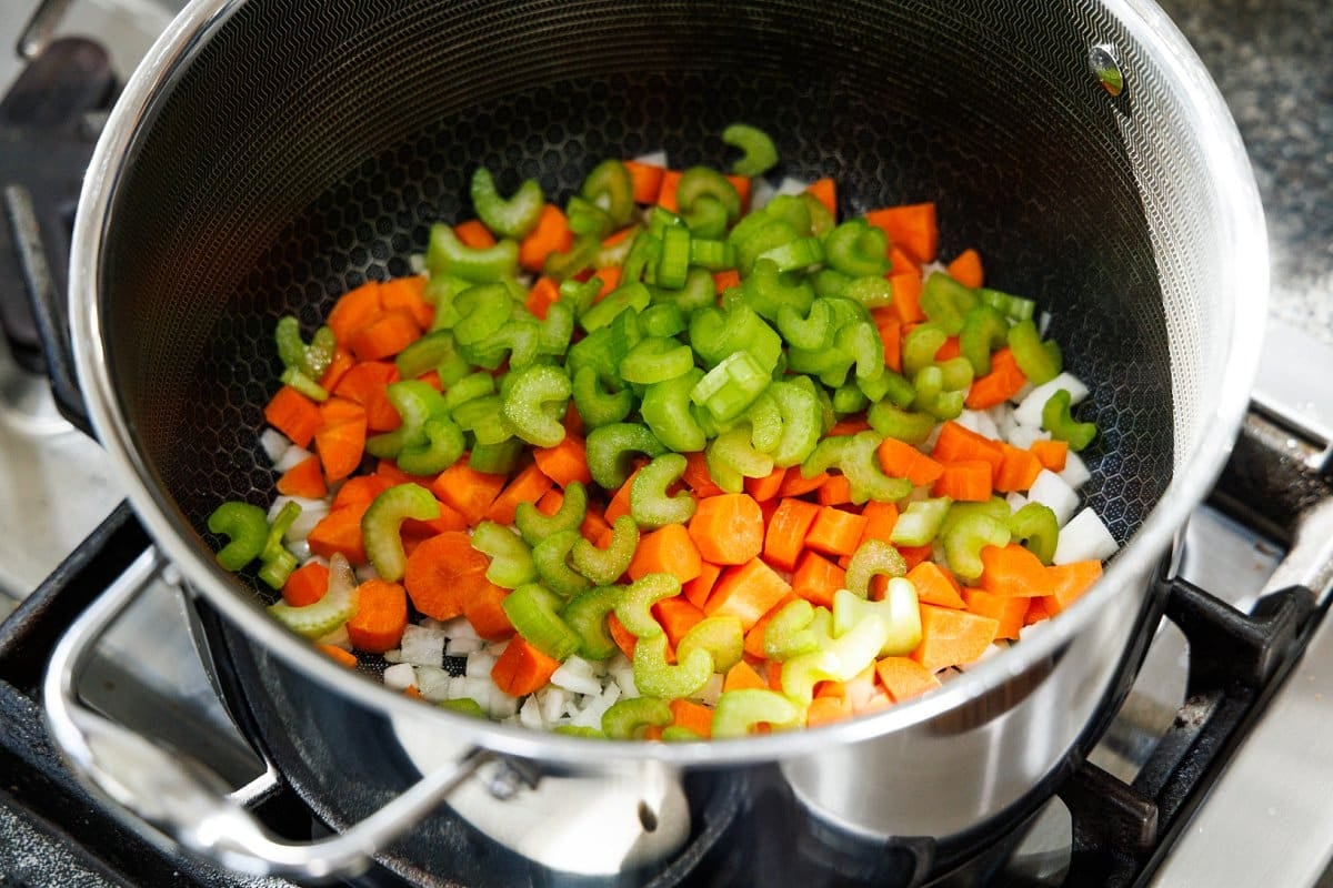 Chopped carrots, celery, and white onion in the bottom of a large, metal soup pot.