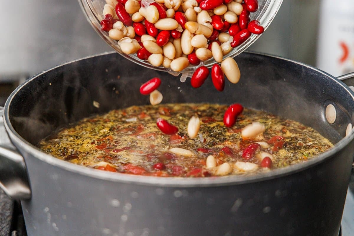 Adding kidney beans and cannellini beans to a pot of soup.