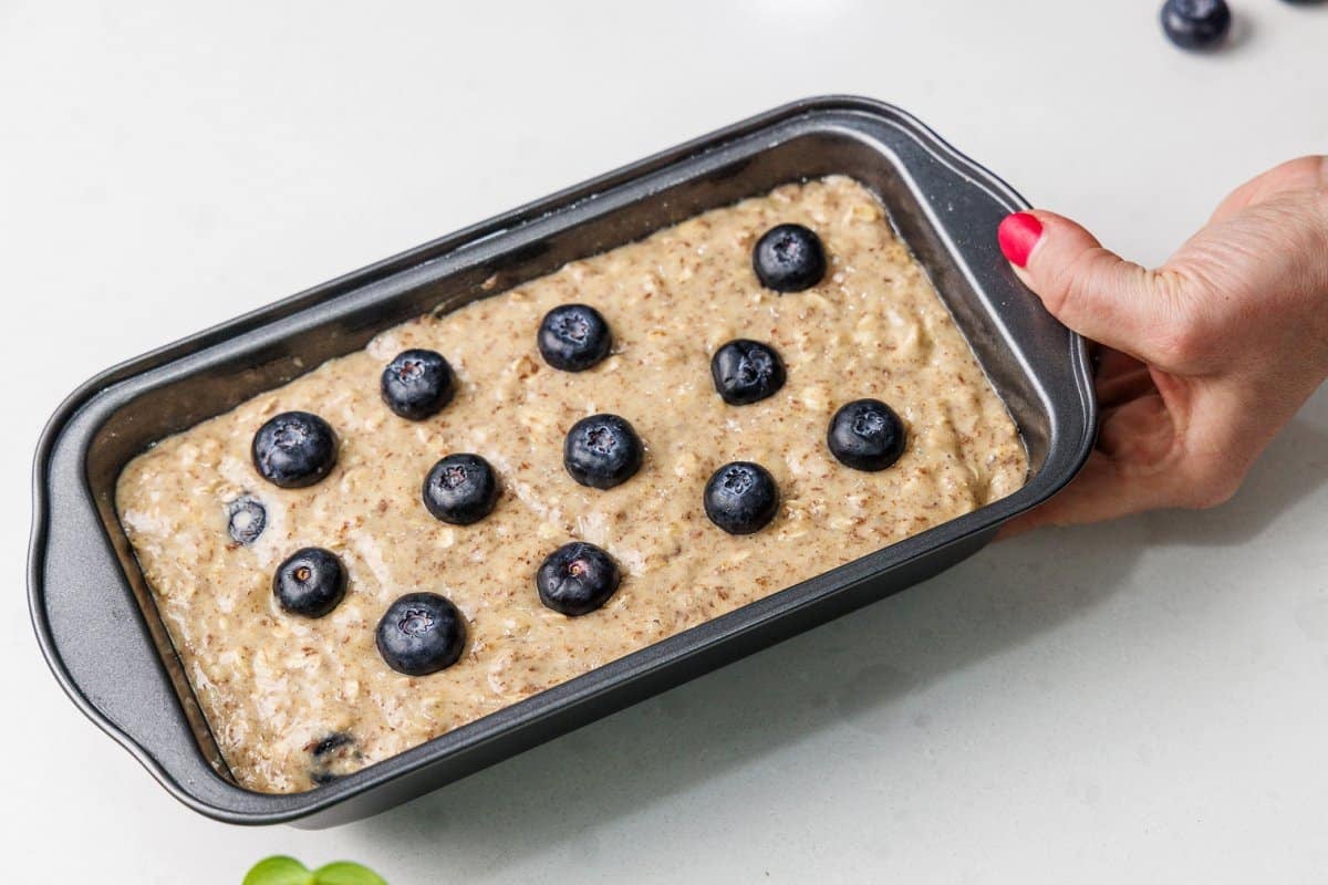 Bread batter in a bread pan with fresh blueberries placed on top.