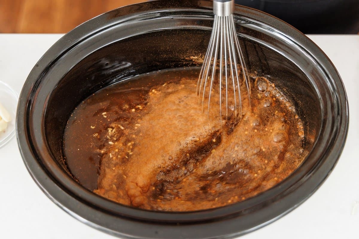 Whisking ingredients for pho-inspired chicken soup in the bowl of a slow cooker.