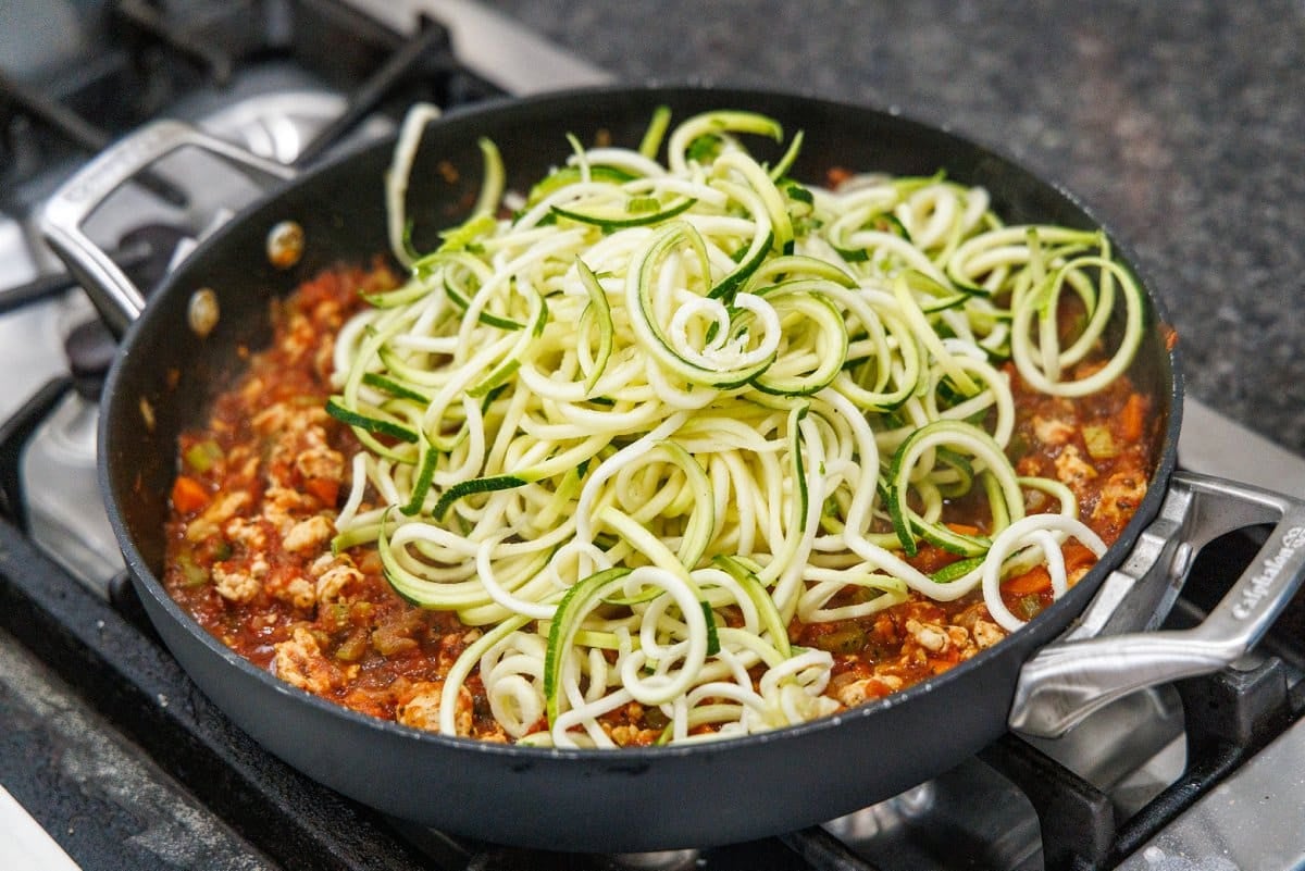 Adding zucchini noodles to bolognese sauce.