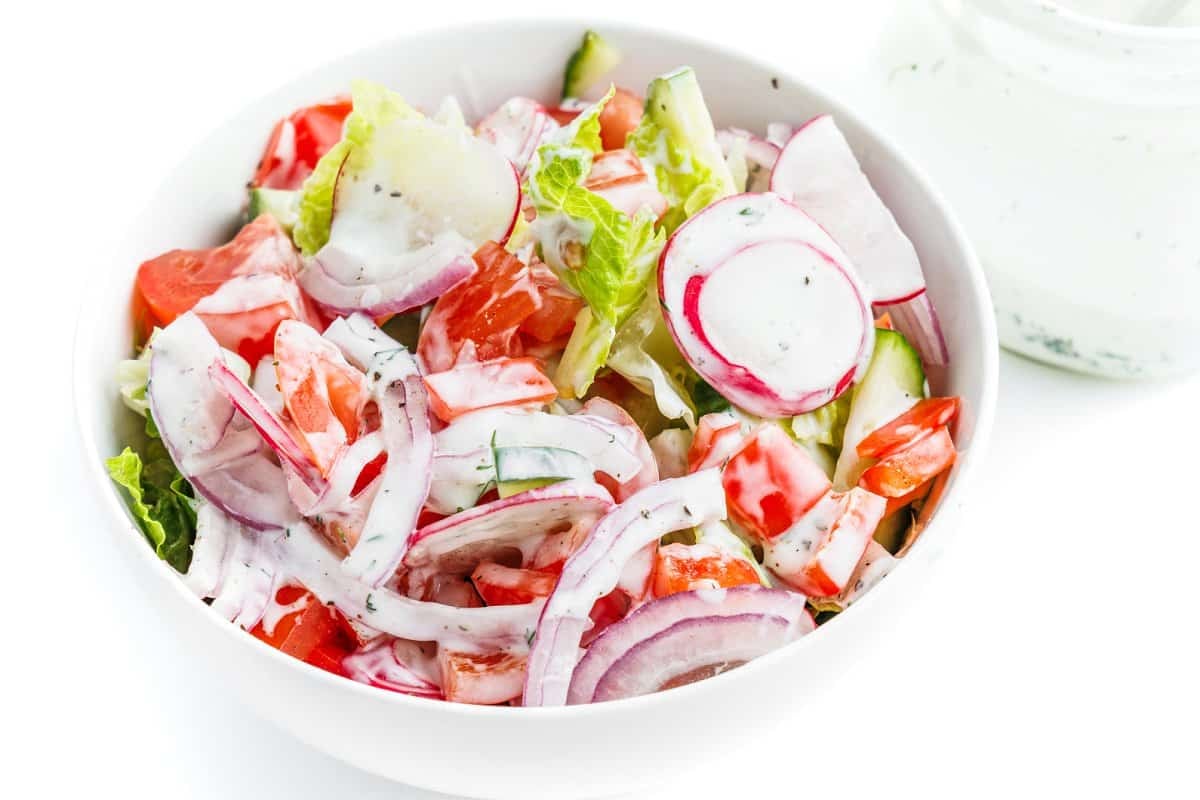 5-ingredient dill ranch dressing poured over the top of a green salad in a white bowl.