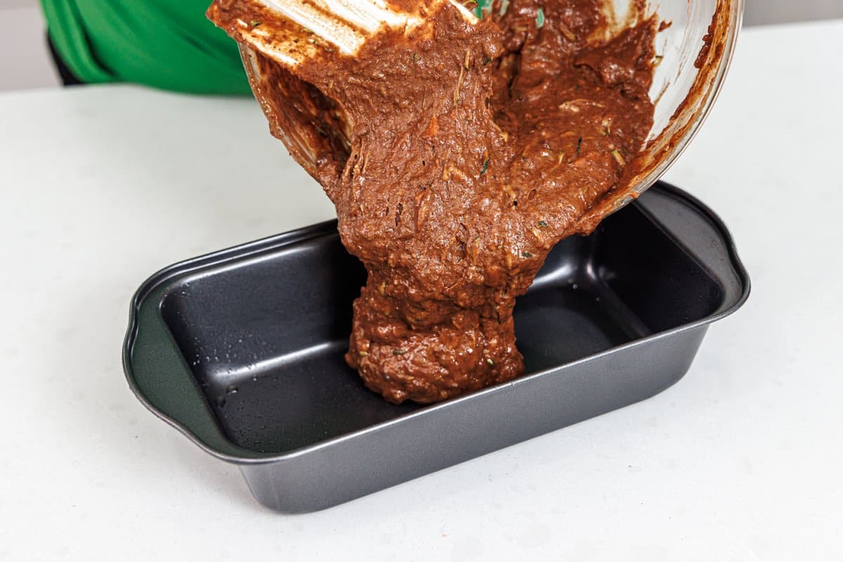 Pouring chocolate bread batter into a prepared bread tin.